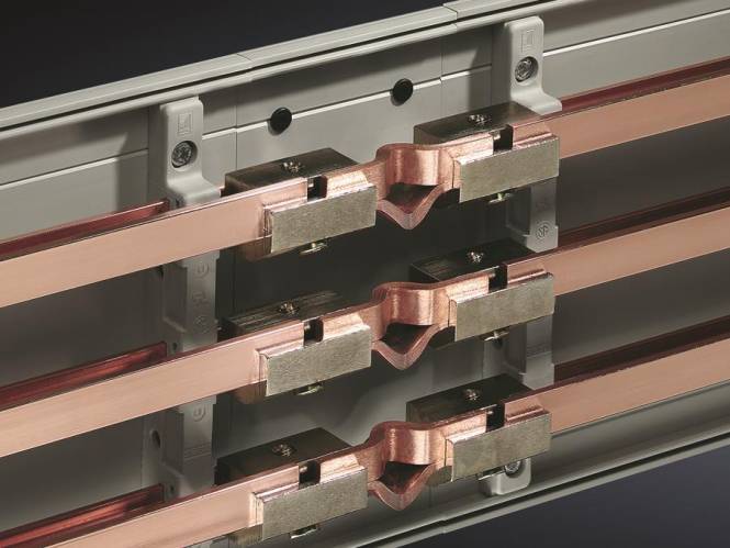 Nahaufnahme eines elektrischen Kupferschienensystems innerhalb einer Schalttafel, das mehrere horizontale Kupferschienen zeigt, die mit Metallklemmen verbunden sind.