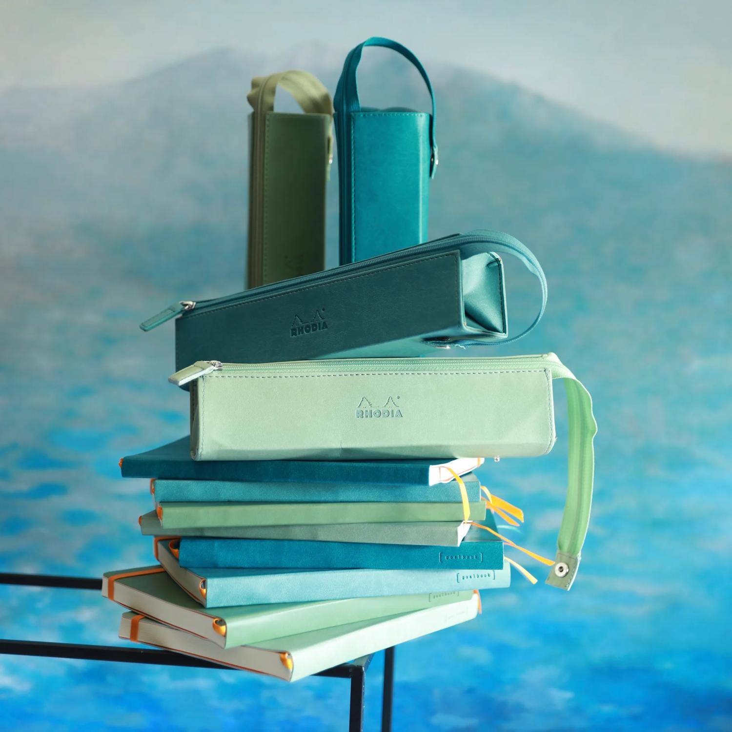 Stapel von bunten Federmäppchen mit Reißverschluss, angeordnet wie Bücher auf einem Regal vor einem blauem Ozean-ähnlichen Hintergrund.