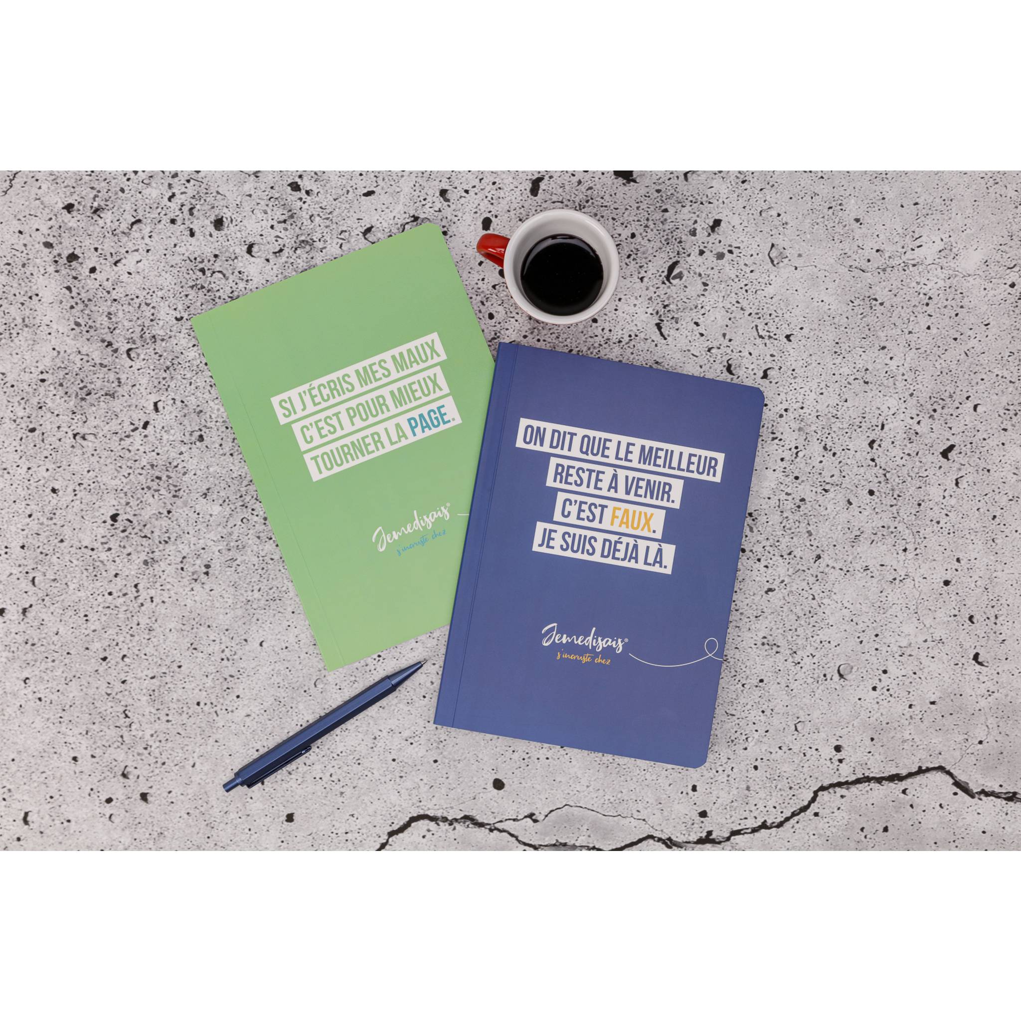 Zwei mit Anführungszeichen bedeckte Notizbücher, eines grün und eines blau, liegen neben einem Stift und einer Kaffeetasse auf einer gesprenkelten Tischplatte.