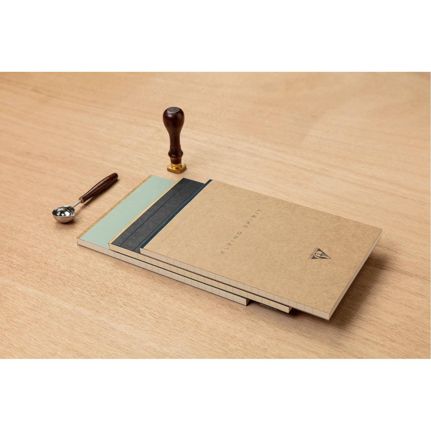 Minimalistische Schreibtischorganizer-Set mit Holzgriff, Löffel und gestapelten Notizbüchern auf einem hellem Holztisch.