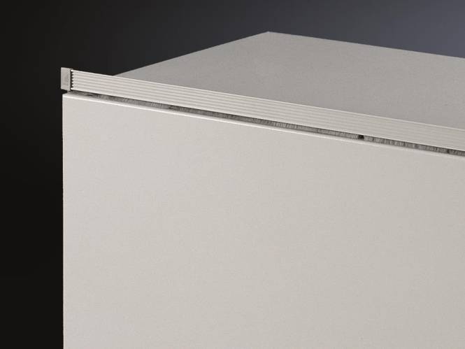 Ein kastenförmiges, hellgefärbtes Objekt mit sichtbaren scharfen Kanten und einer glatten Oberfläche, vor einem dunklen Hintergrund angebracht.