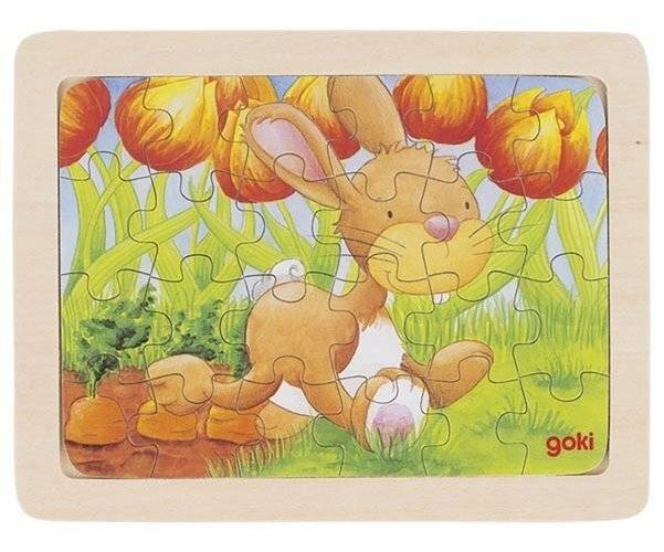 Ein Hase, der eine Karotte hält, läuft durch einen Garten mit bunten Tulpen im Hintergrund. Die Szene ist auf einem Kinderpuzzle dargestellt.