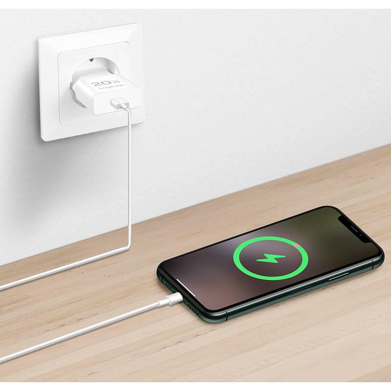 Ein Smartphone auf einer Holzoberfläche wird geladen, mit einem weißen Kabel an eine Wandsteckdose angeschlossen, wobei eine grüne Ladestatusanzeige zu sehen ist.