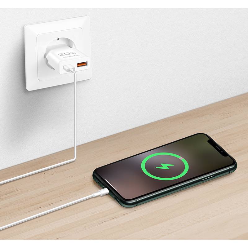 Ein Smartphone liegt auf einer Holzoberfläche und ist über ein Kabel mit einem Wandsteckdosenadapter verbunden. Auf dem Bildschirm wird ein Ladesymbol angezeigt.