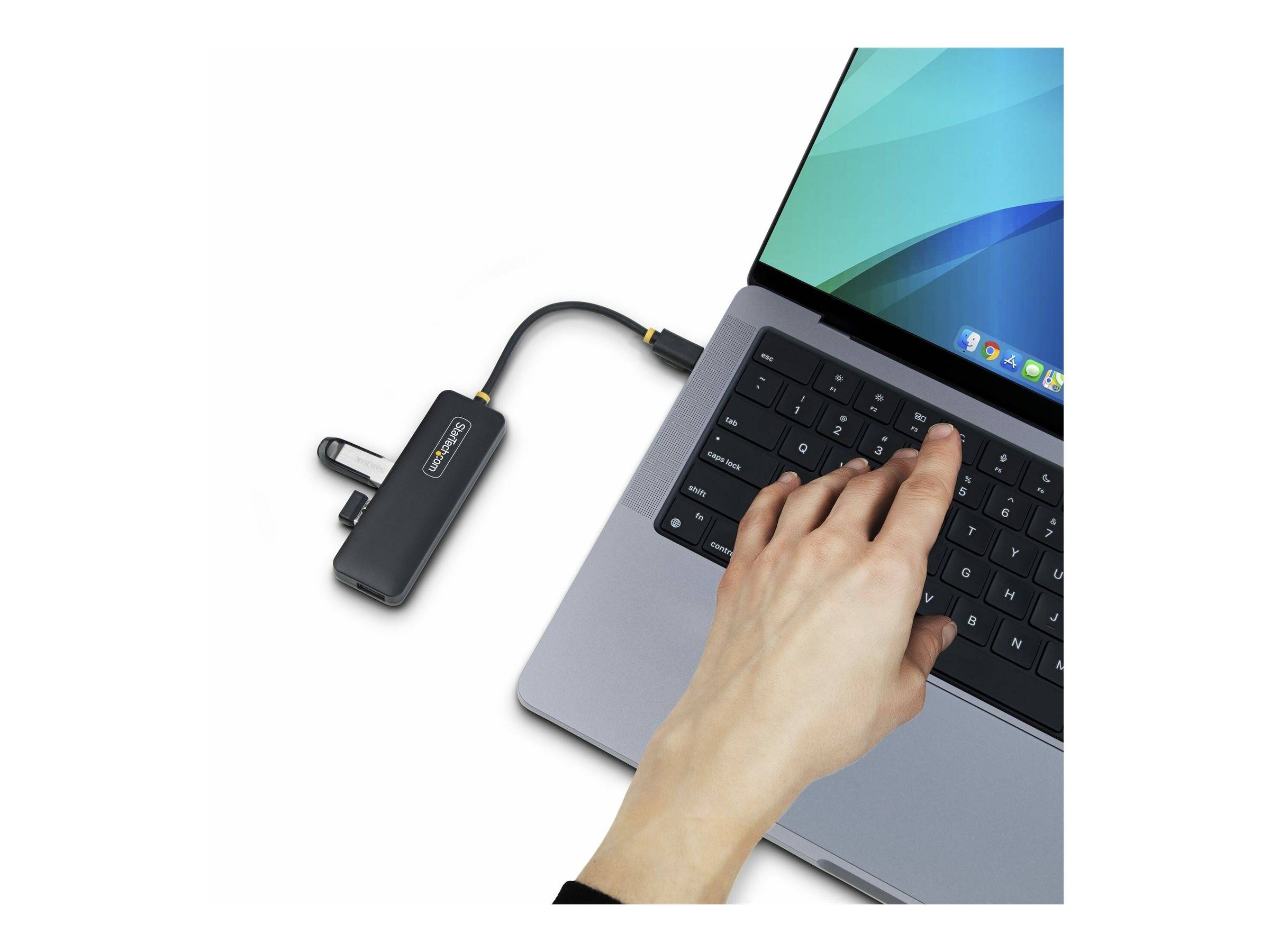 Hand steckt einen USB-C-Hub/Dongle in einen Laptop, wobei der Laptop-Bildschirm eingeschaltet ist und einen weißen Hintergrund hat.
