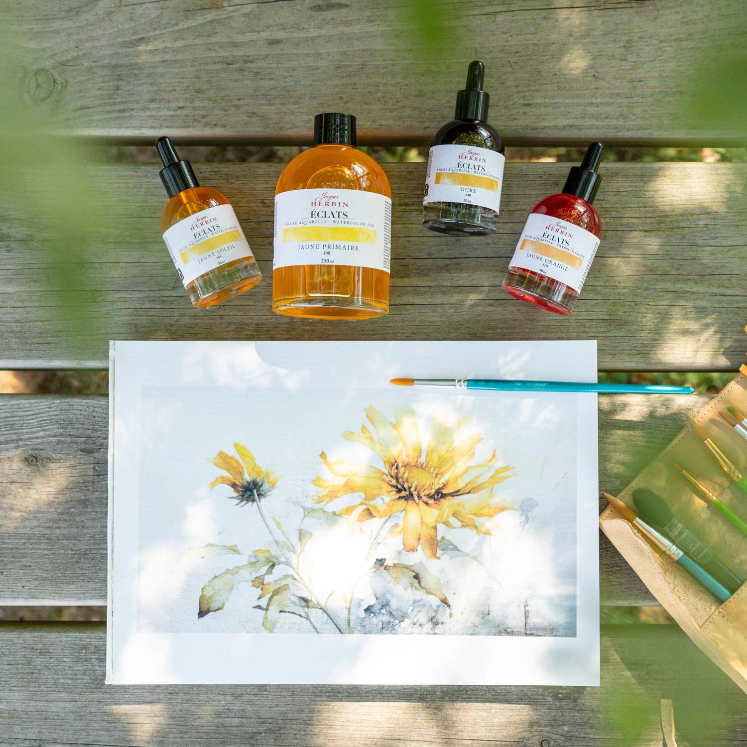 Gemälde einer Sonnenblume auf einer Holzoberfläche, umgeben von vier Tintenfläschchen in Orange-, Schwarz- und Rottönen, neben einem Pinsel.