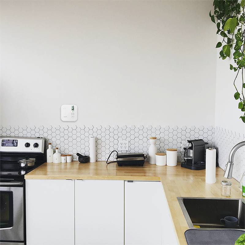 Minimalistische Küche mit weißen Schränken, sechseckiger Fliesenwandverkleidung, Herd, Kaffeemaschine, Spüle und einer großen leeren Wand über der Arbeitsplatte.