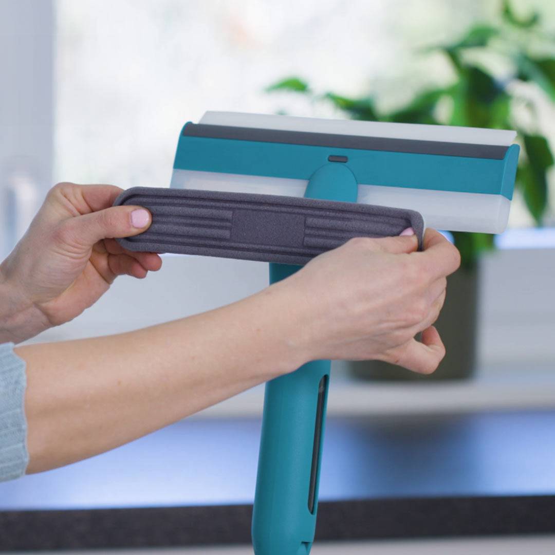 Eine Person hält ein Reinigungswerkzeug und stellt es ein oder montiert es in einer häuslichen Umgebung in der Nähe eines Fensters mit unscharfem grünem Hintergrund.