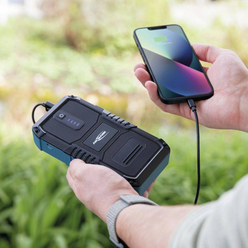 Eine Person, die ein Smartphone von einer robusten tragbaren Anker-Powerbank im Freien auflädt.
