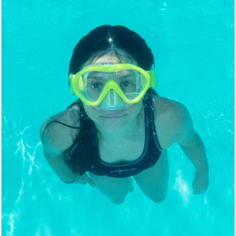 Eine Person in Schwimmausrüstung ist unter Wasser mit einer Schnorchelmaske, blickt zur Kamera und ist von klarem, blauem Wasser umgeben.