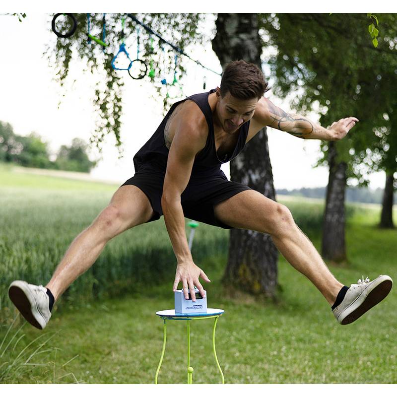 Ein Mann balanciert geschickt auf einer Slackleine in einem Park, umgeben von Bäumen und Gras, wobei er Beweglichkeit und Konzentration zur Schau stellt.