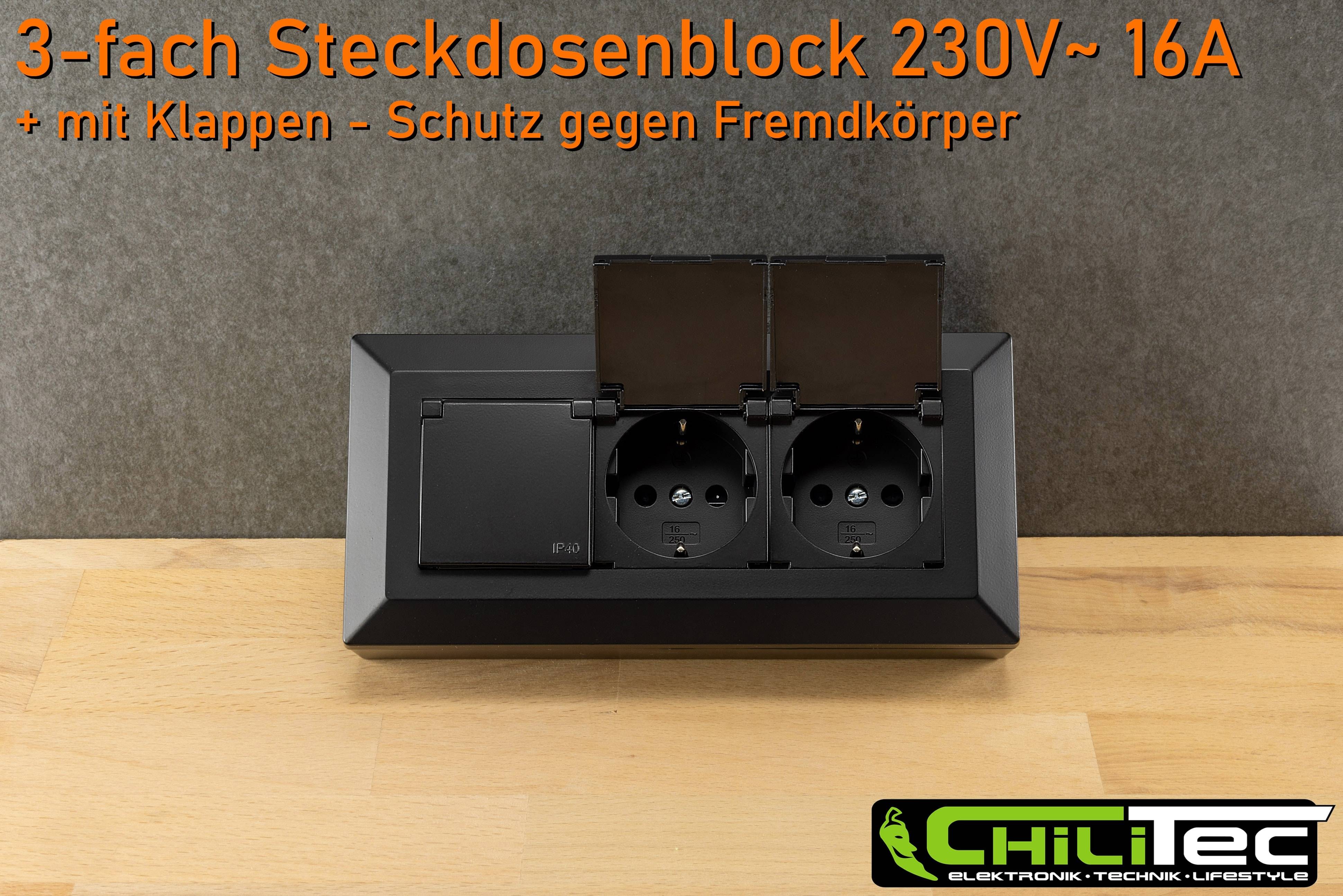 Eine schwarze Doppelsteckdose mit Schutzabdeckungen, beschriftet mit 'Steckdosenblock 230V~', vor einem grauen Hintergrund und Holzoberfläche.