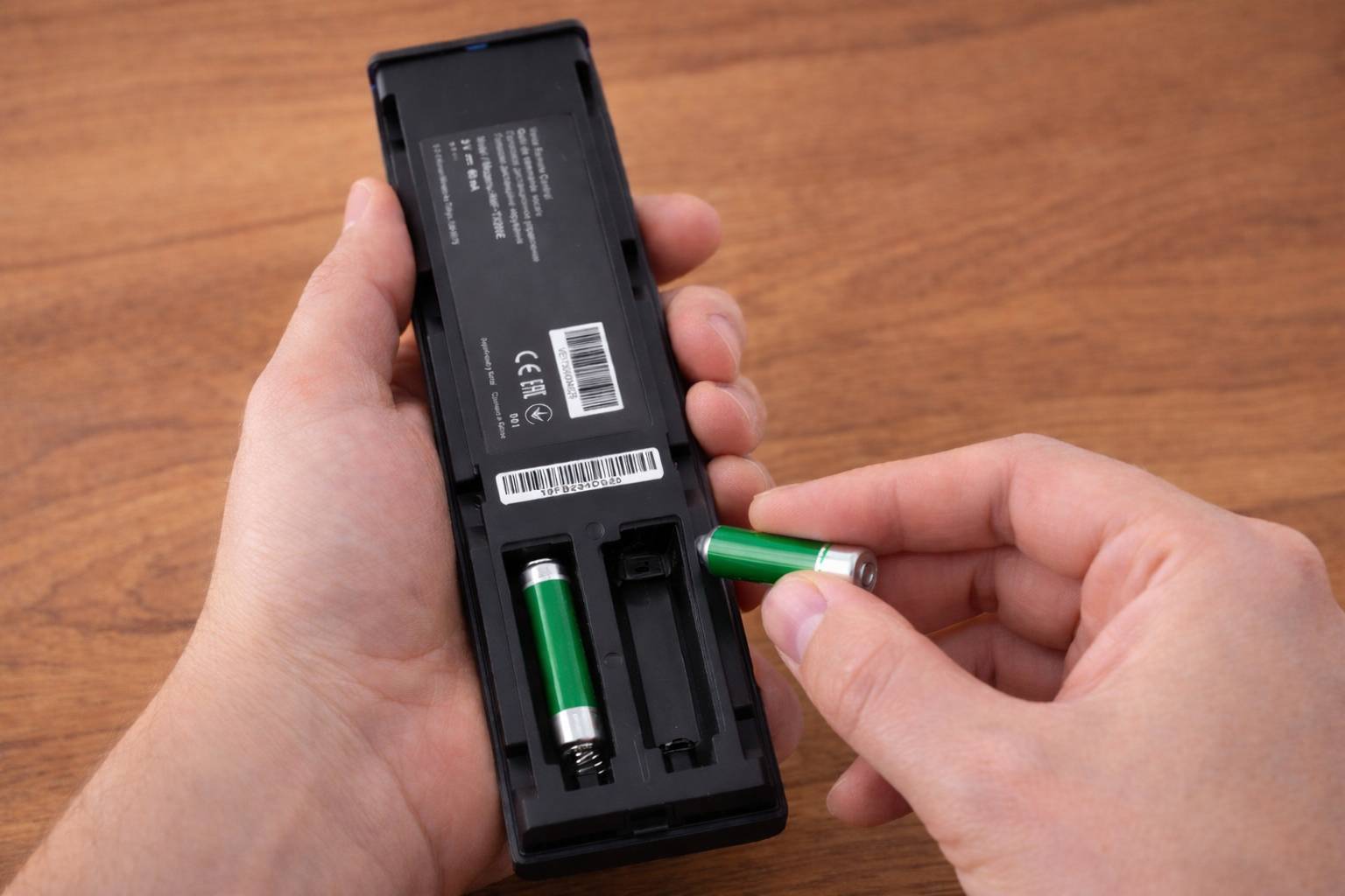 Hände, die Batterien in eine schwarze Fernbedienung auf einer Holzoberfläche einsetzen.