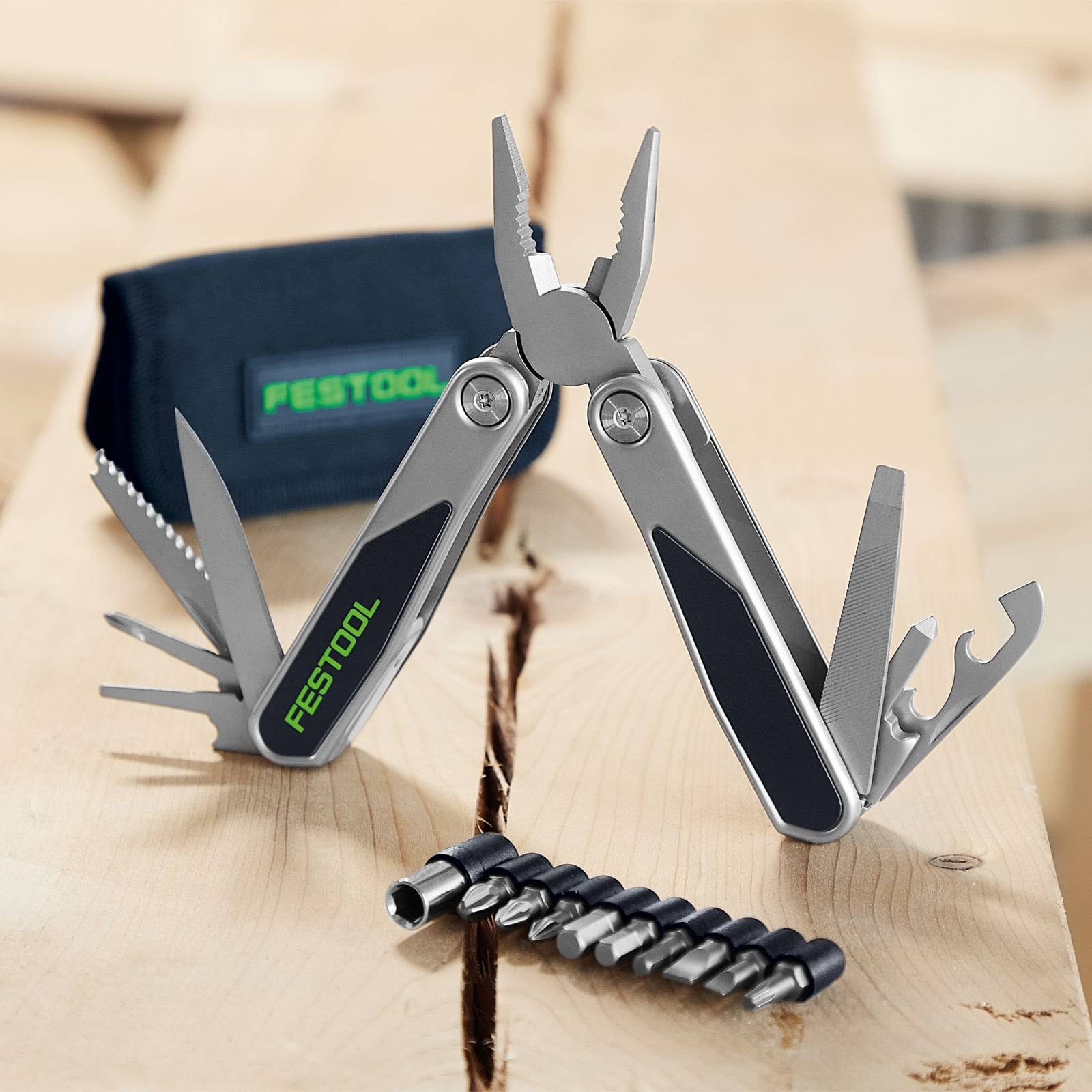 Ein Multitool mit verschiedenen geöffneten Werkzeugen, ein Festool-Koffer und eine Reihe von Schrauberbit-Einsätzen auf einer Holzoberfläche.