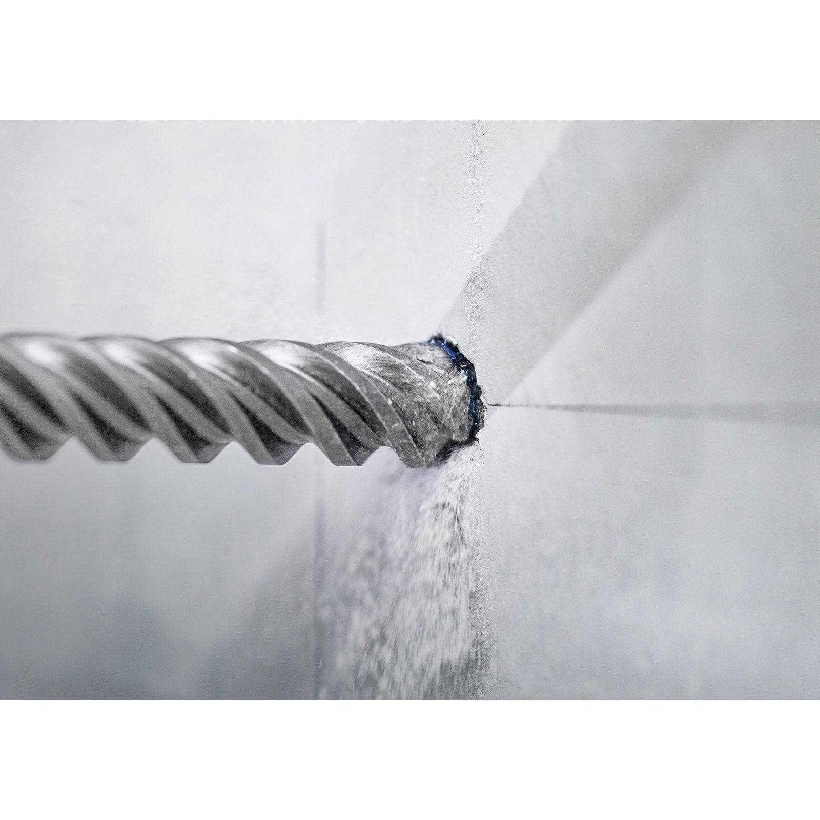 Eine Bohrerspitze, die ein Loch in eine weiße Wand bohrt, mit sichtbaren Staubpartikeln, die von der Kontaktstelle herabfallen.