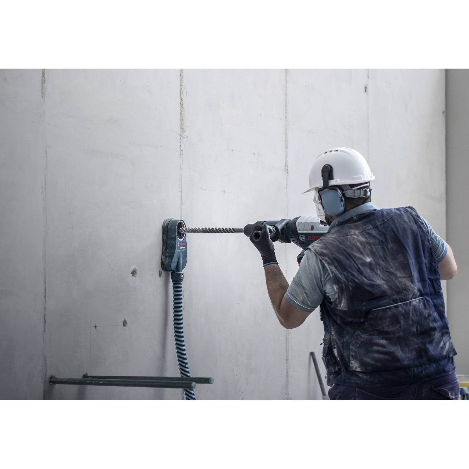 Ein Bauarbeiter mit Helm und Handschuhen bohrt in eine Betonwand und konzentriert sich auf seine Aufgabe, wobei er größte Präzision walten lässt.