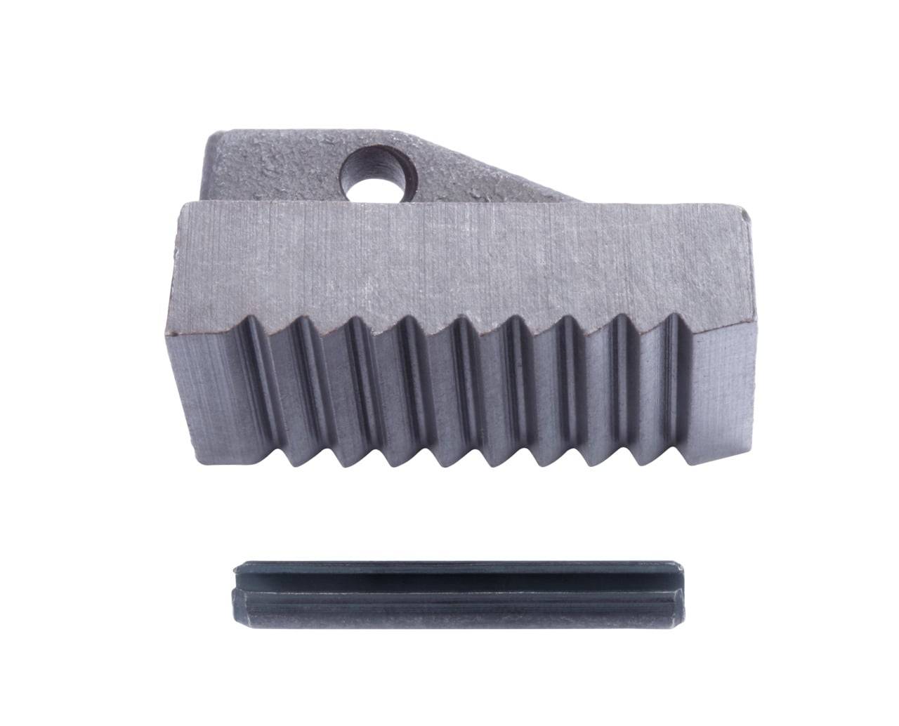 Ein Metallblock mit einem großen Rillenmuster sitzt über einem schmalen, flachen Metallstück. Der Block hat auf einer Seite ein Loch, was auf eine Befestigungsmöglichkeit hindeutet.