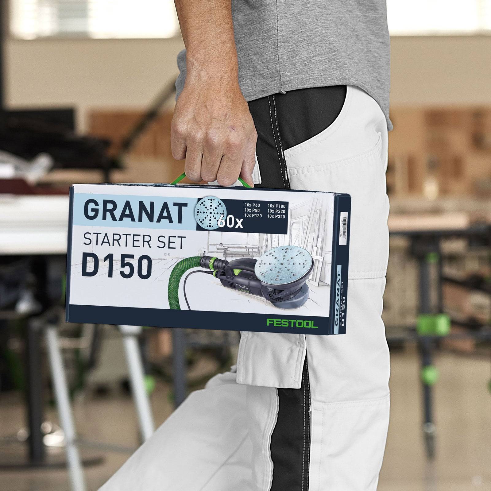 Eine Person, die einen Festool Granat Starter-Satz D150-Box trägt, der ein Schleifwerkzeug und Schleifscheiben in einer Werkstattumgebung zeigt.