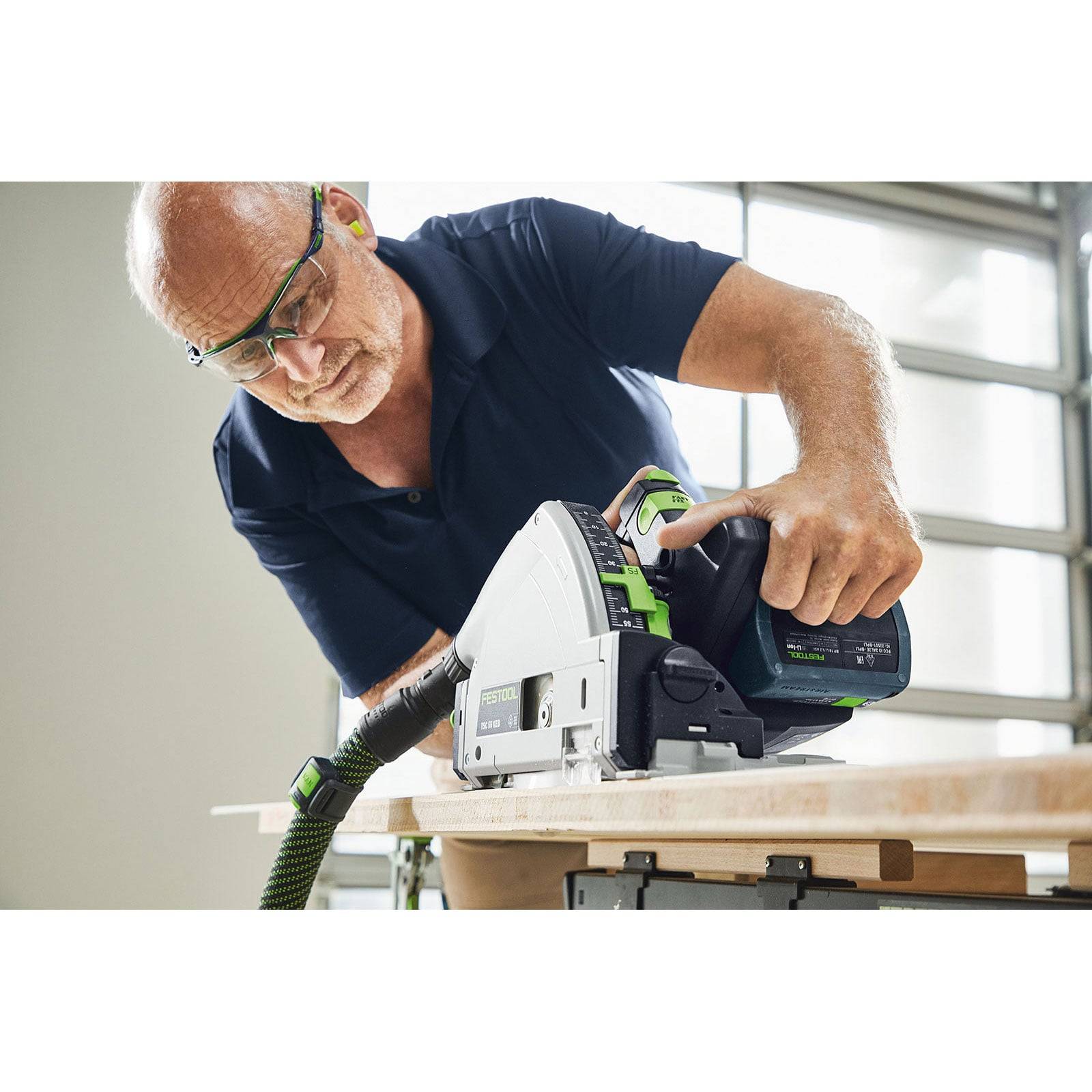 Eine Person mit Schutzbrille verwendet eine Kreissäge, um ein Holzstück auf einer Werkbank zu sägen und konzentriert sich dabei voll und ganz auf die Aufgabe.