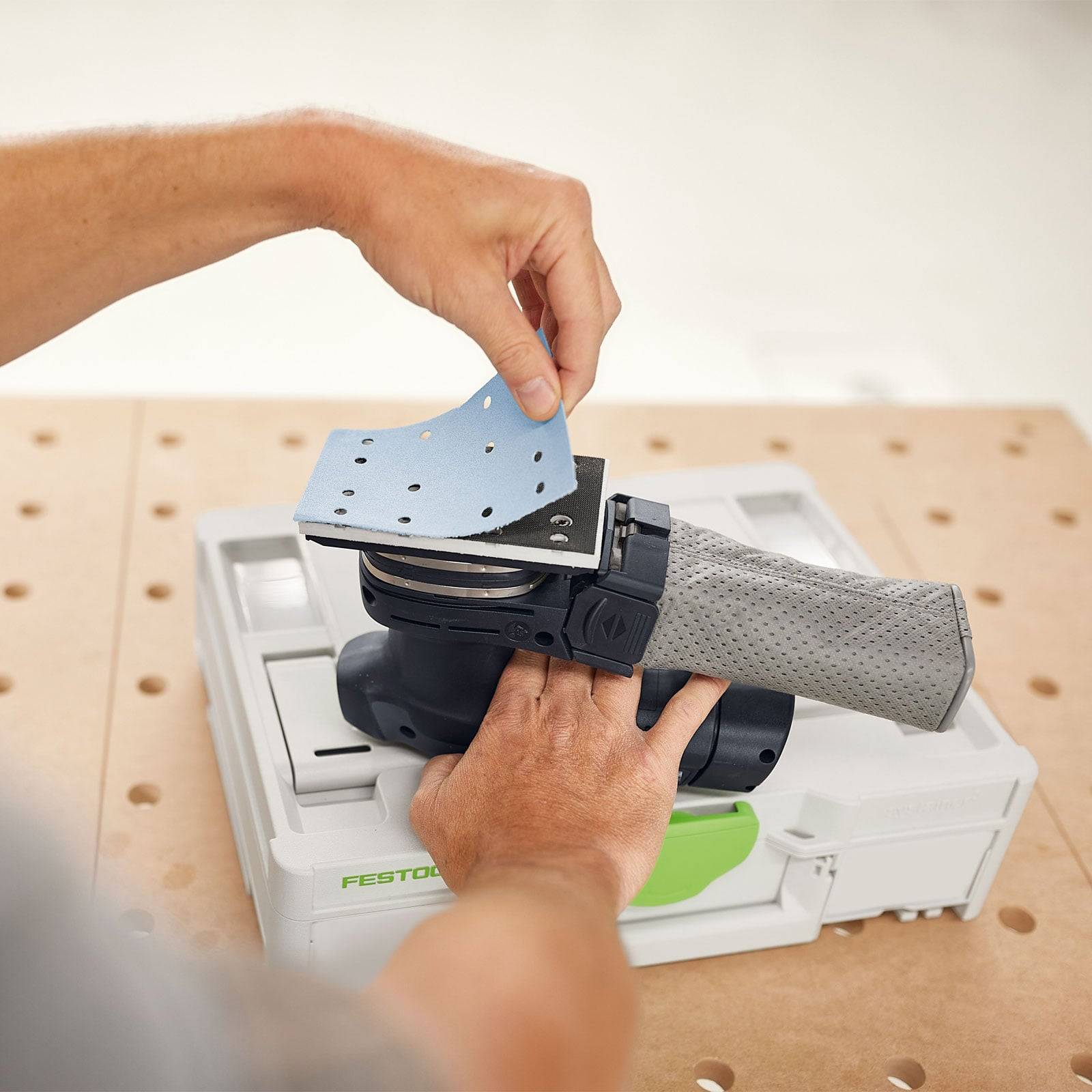 Eine Person wechselt Schleifpapier an einem elektischen Schleiffer und zeigt die Werkzeugwartung auf einer perforierten Oberfläche.