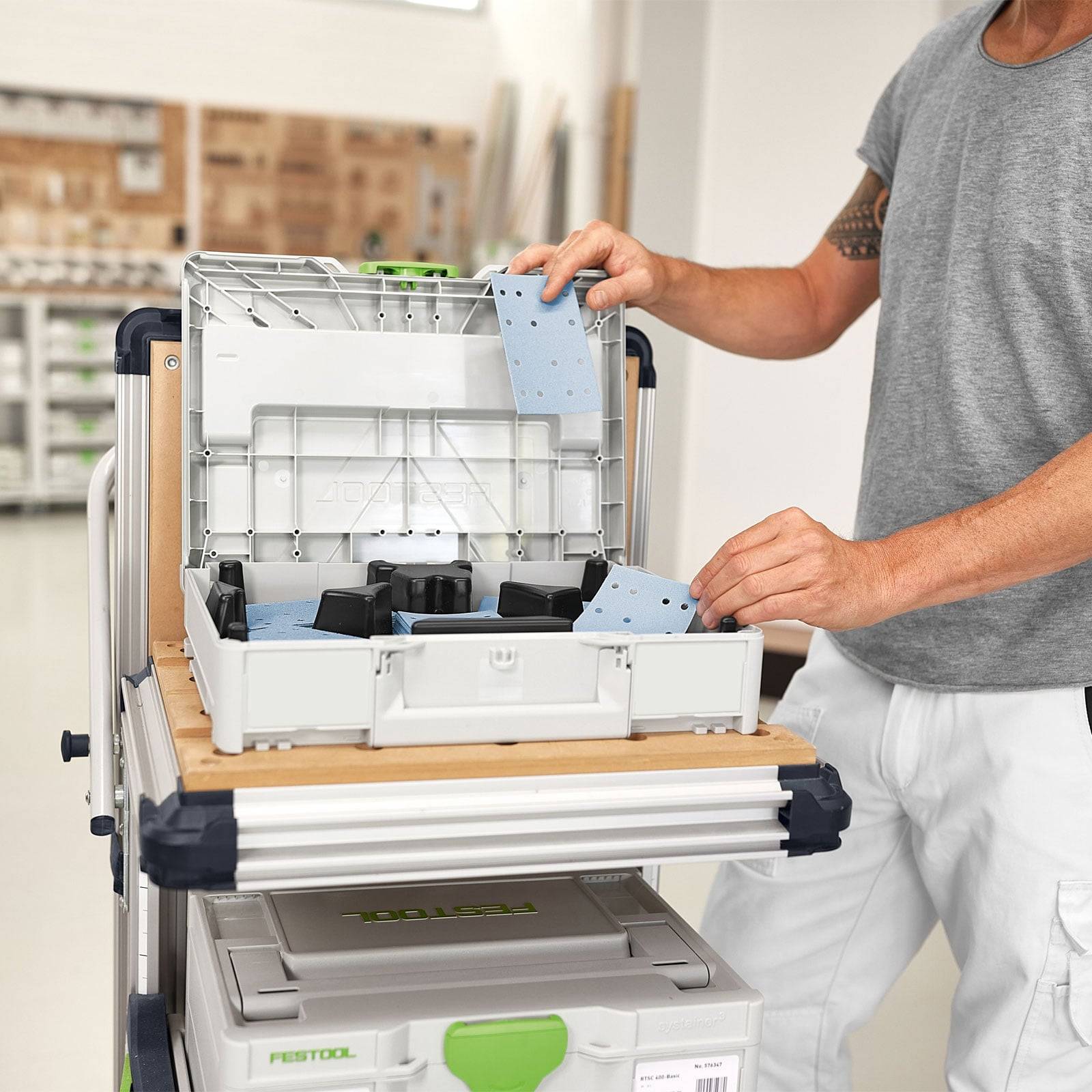 Eine Person ordnet kleine Werkzeuge in einer Werkstattspeicherkiste an, während sie neben einem Stapel von Werkzeugkästen steht.
