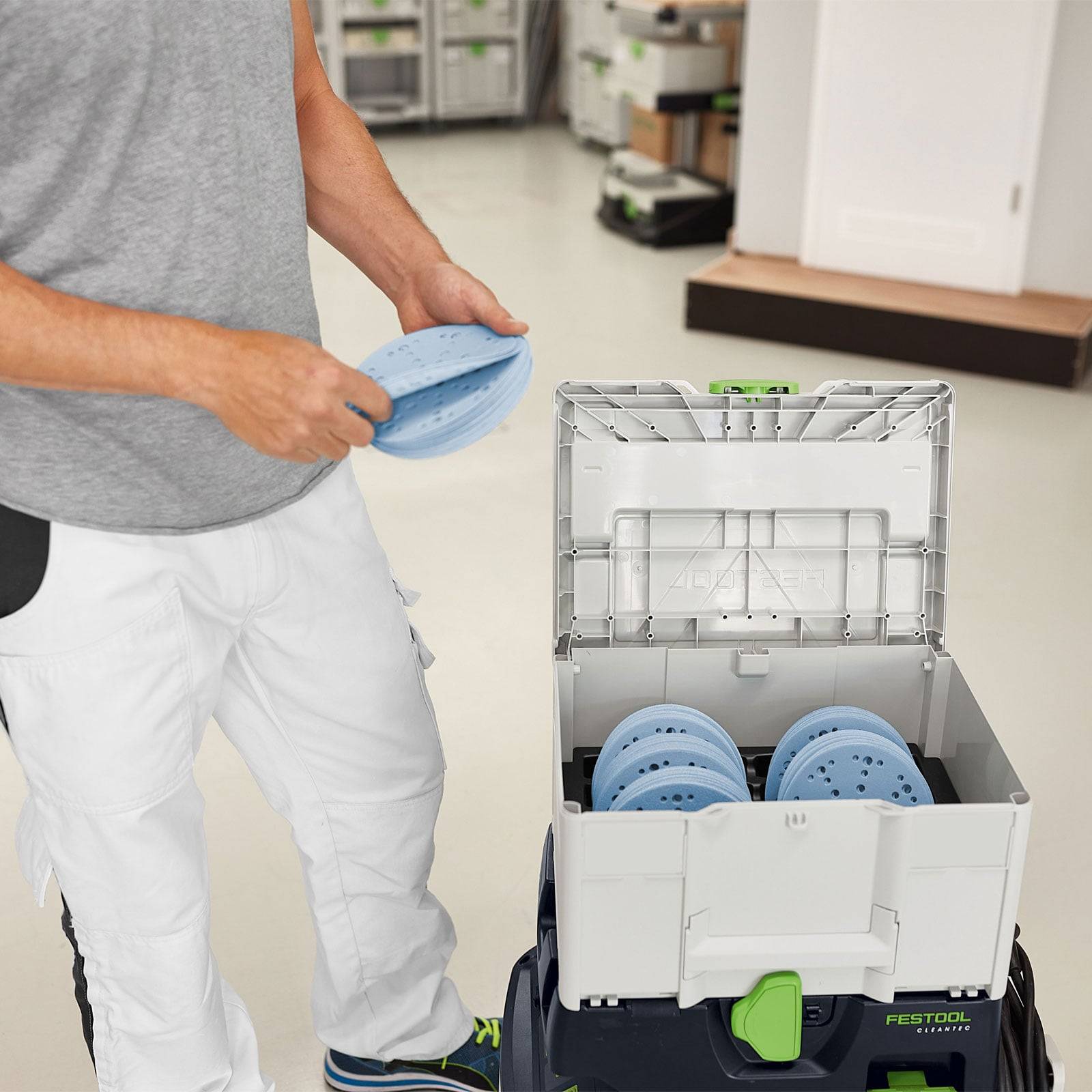 Eine Person ordnet blaue Schleifscheiben in einen Aufbewahrungsbehälter in einer Werkstattumgebung an und demonstriert damit die Organisation von Werkzeugen.