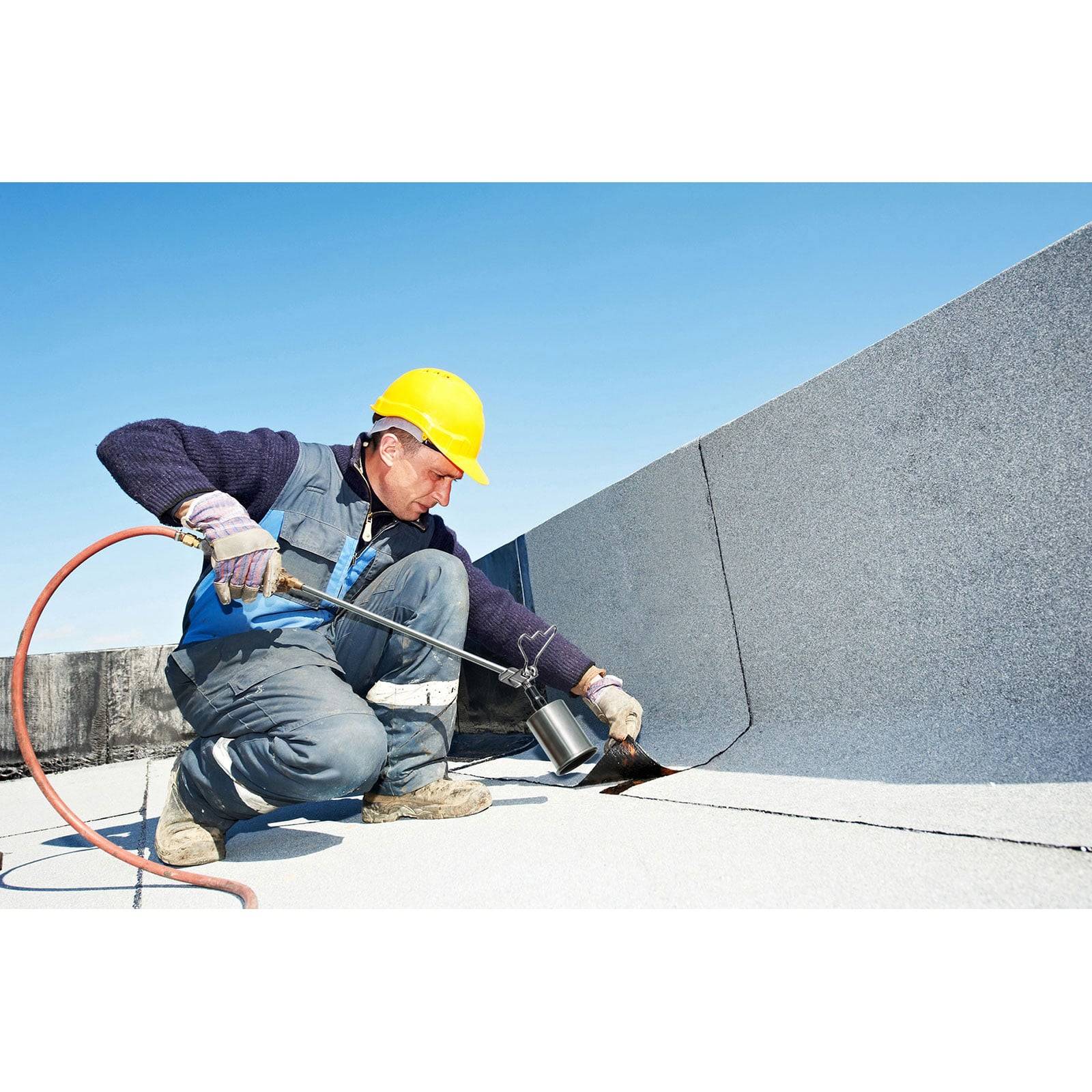 Ein Arbeiter in Schutzausrüstung verwendet eine Heißluftpistole an Dachmaterialien unter einem klaren blauen Himmel, was auf eine Dachmontage oder -wartung hinweist.
