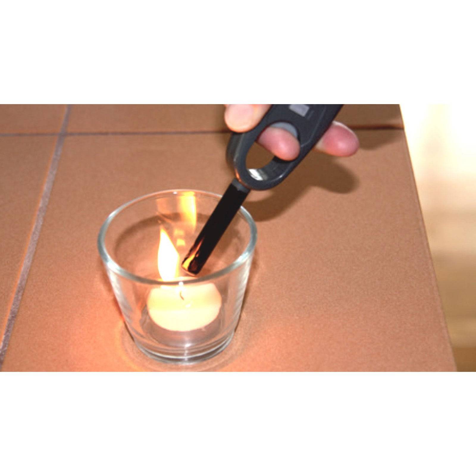 Eine Hand, die einen langen Feuerzeiger verwendet, um eine kleine Kerze in einem Glashalter auf einem braunen Tisch anzuzünden.