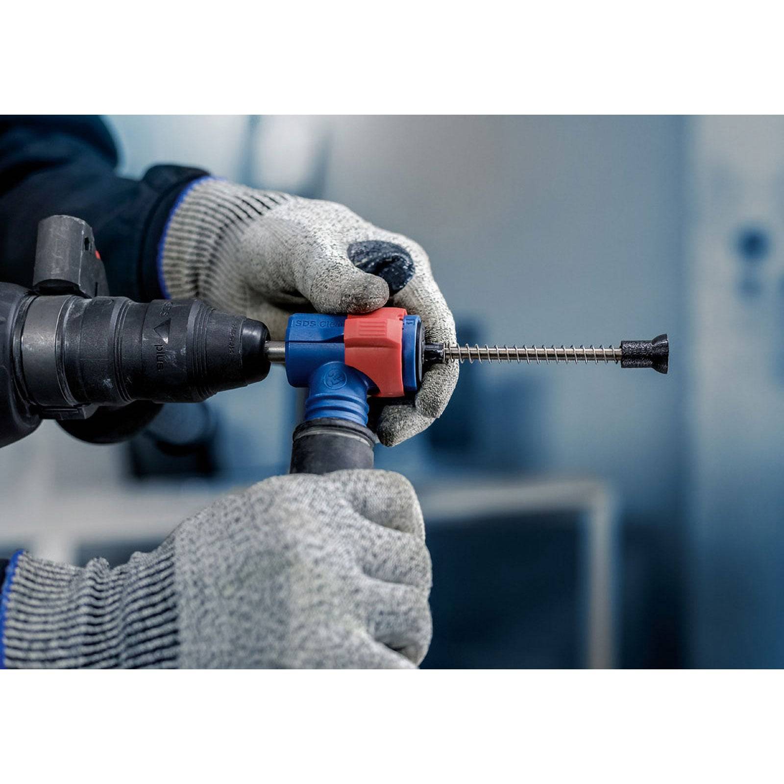 Eine Person mit Schutzhandschuhen benutzt eine Bohrmaschine mit blauem und rotem Zubehör.