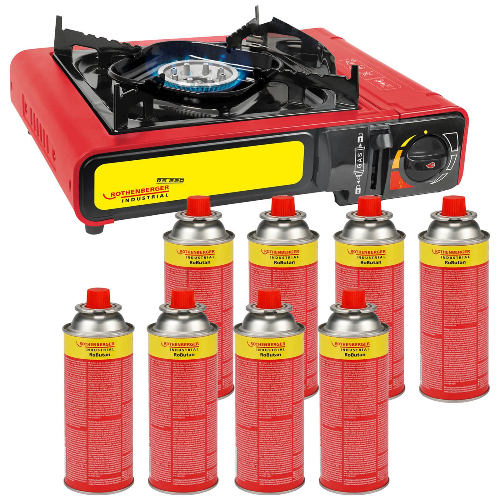 Roter Campingkocher mit brennendem Brenner, umgeben von acht Treibstoffkanistern. Der Kocher ist kompakt und tragbar, geeignet für den Einsatz im Freien.