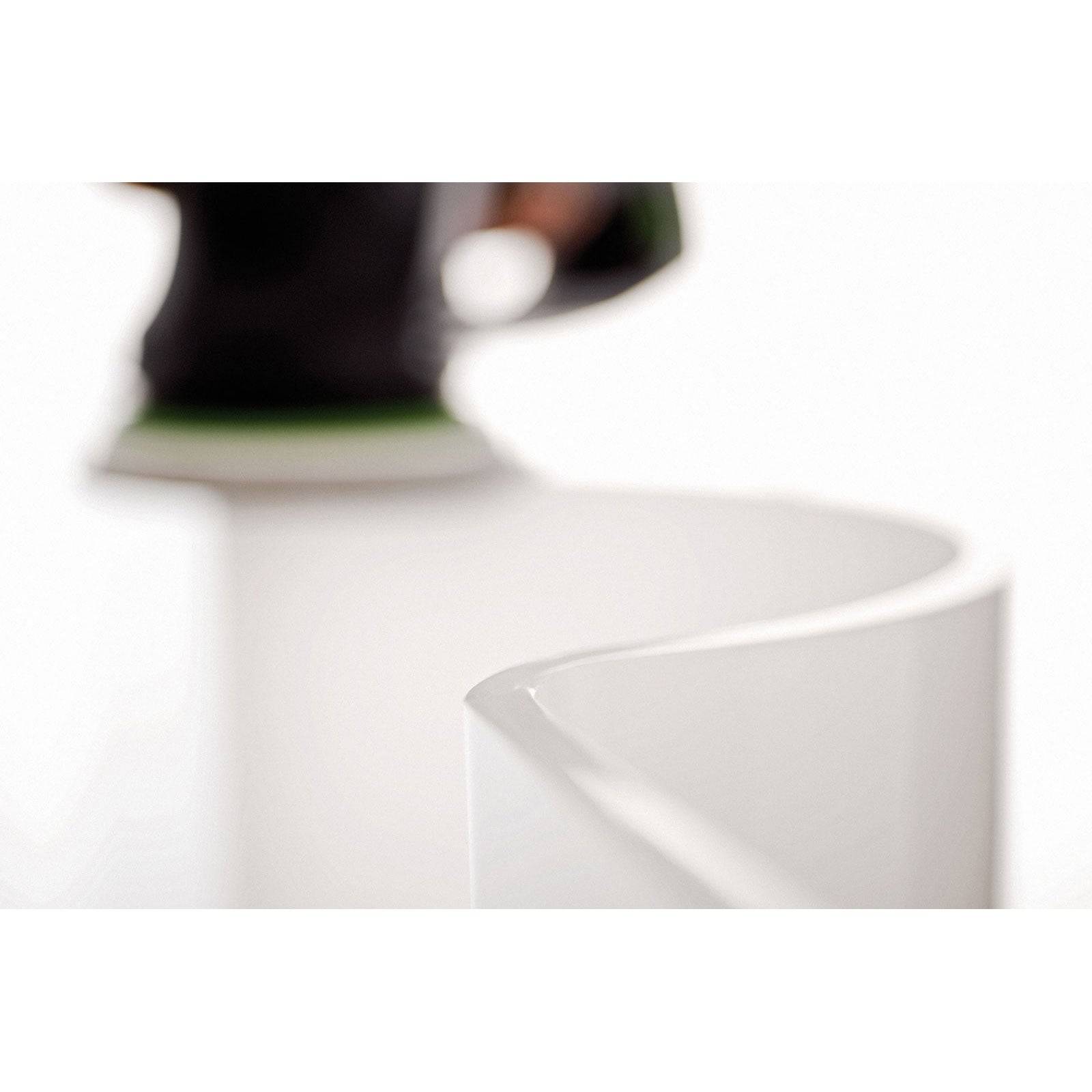 Nahaufnahme einer weißen, geschwungenen Keramiktasse mit unscharfem Hintergrund, die sich auf die Kante der Tasse konzentriert und deren glatte Gestaltung hervorhebt.