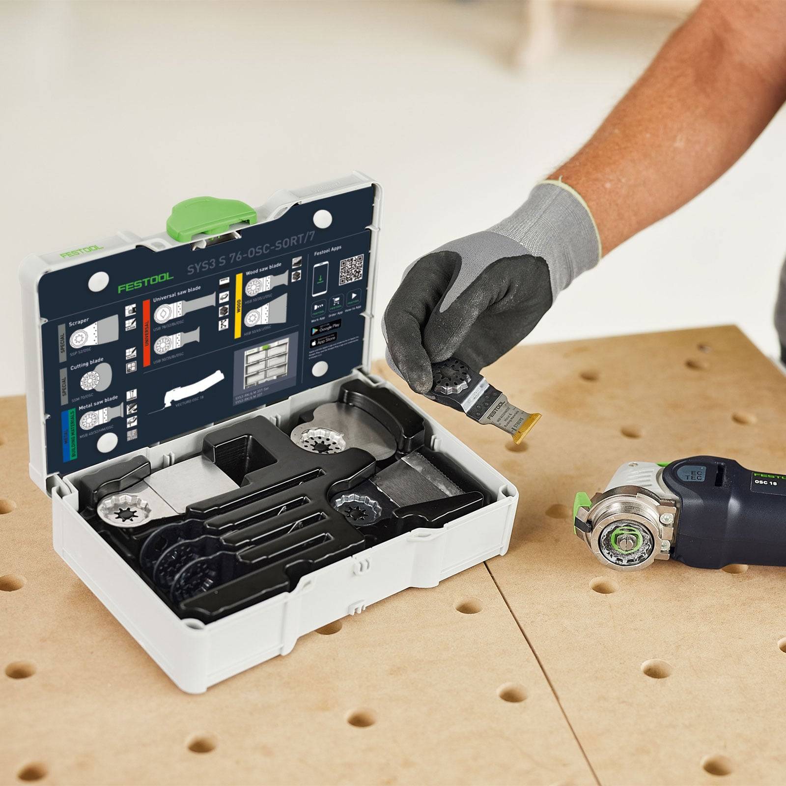 Eine Person mit Handschuh wählt ein oszillierendes Werkzeugzubehör aus einem Etui mit verschiedenen Aufsätzen, neben einem Multitool.