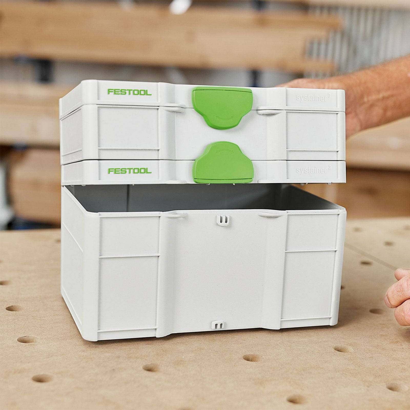 Ein Stapel von Festool-Lagerkästen mit grünen Griffen, dargestellt auf einer perforierten Werkbankoberfläche, Teil einer Werkstattumgebung.