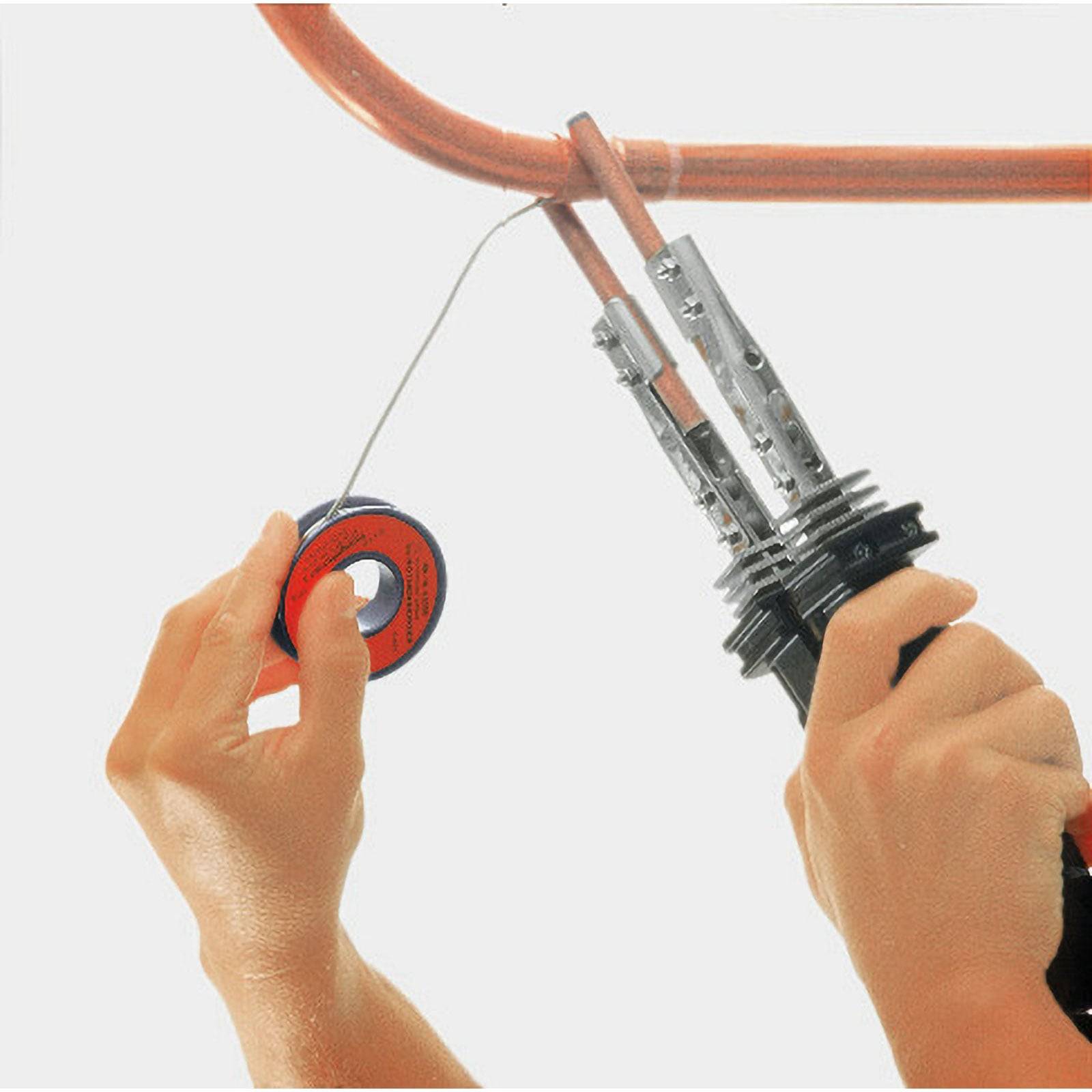 Hände halten ein Lötkolben und Lötzinn und löten eine Rohrverschraubung.