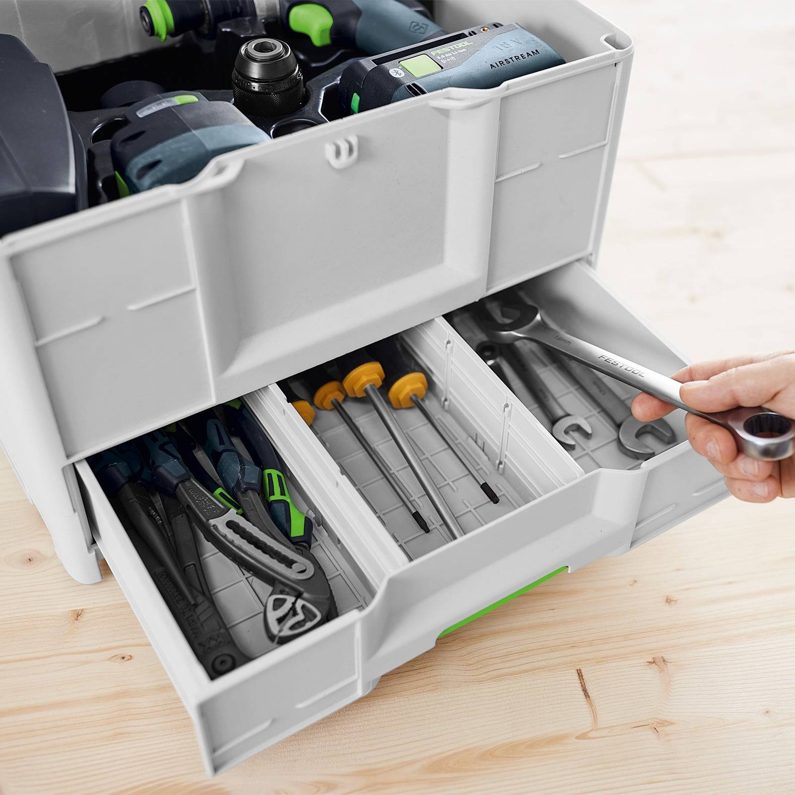 Eine Hand, die nach einem Schraubenschlüssel in einer organisierten Werkzeugschublade greift, die verschiedene Werkzeuge enthält, einschließlich Bohrteile und Schraubendreher.