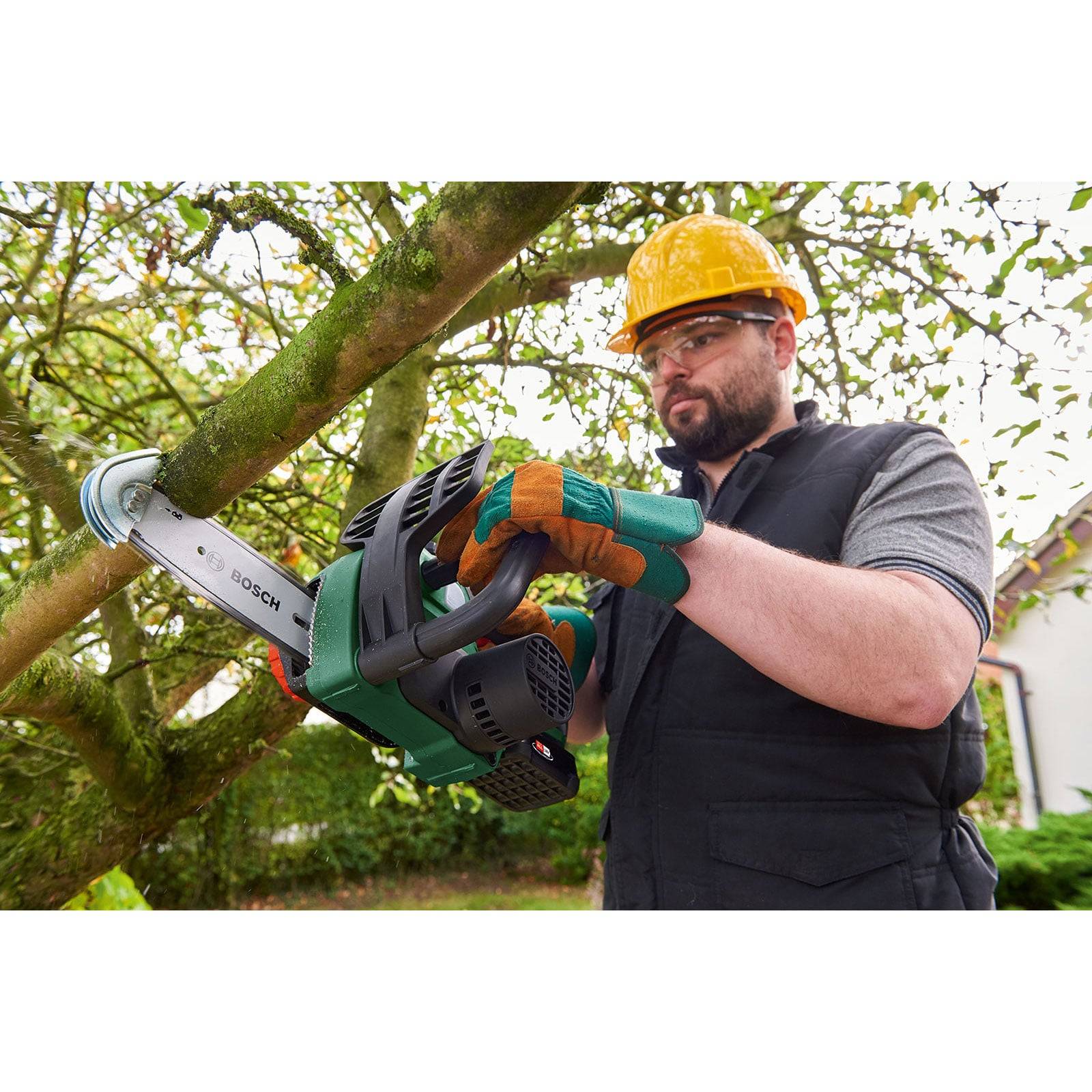Eine Person in Sicherheitsausrüstung, einschließlich Helm und Handschuhen, verwendet eine Bosch-Kettensäge, um einen Baumast im Freien zu zersägen.