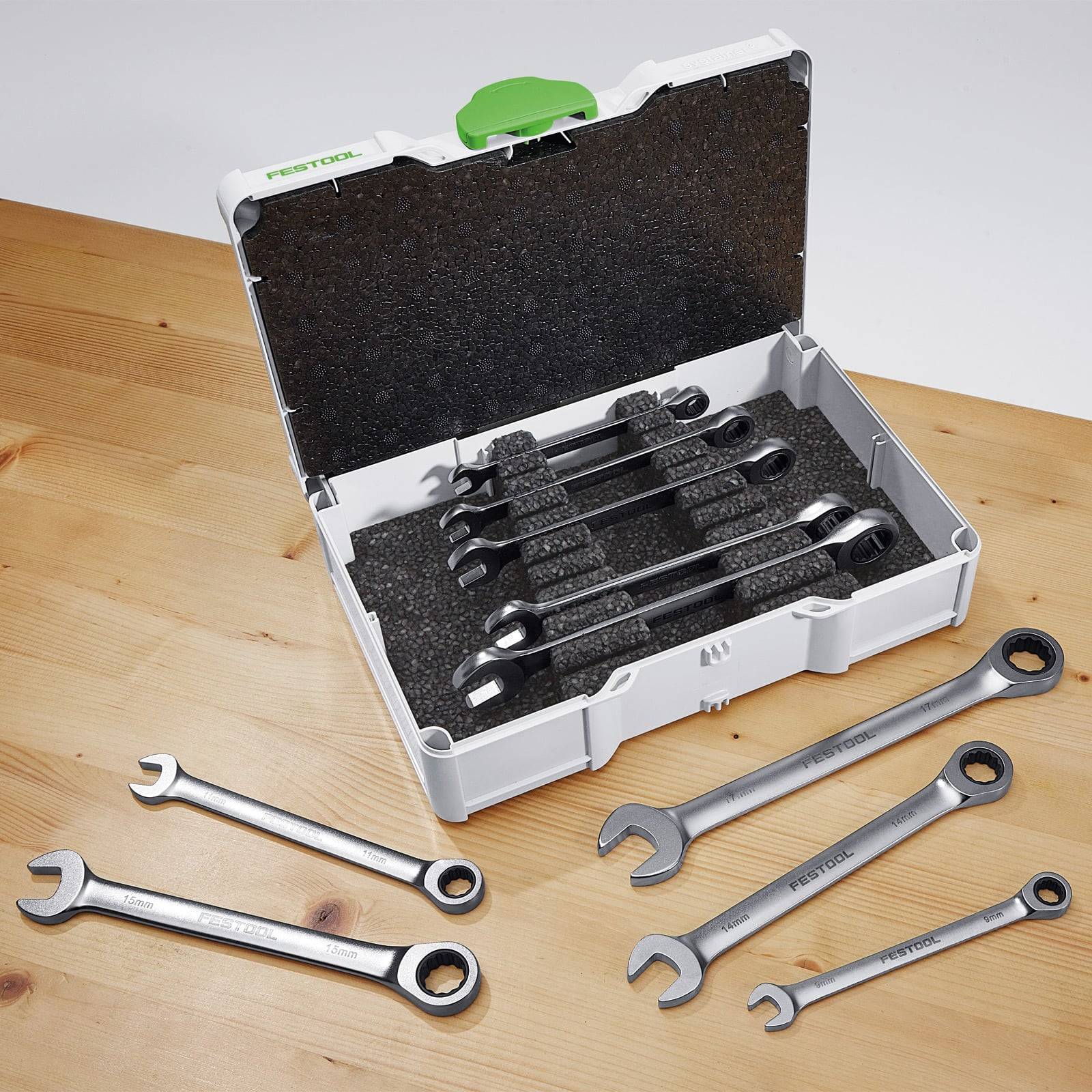 Eine offene Werkzeugkiste mit mehreren Schraubenschlüsseln unterschiedlicher Größen, die innen und auf einer Holzoberfläche angeordnet sind.