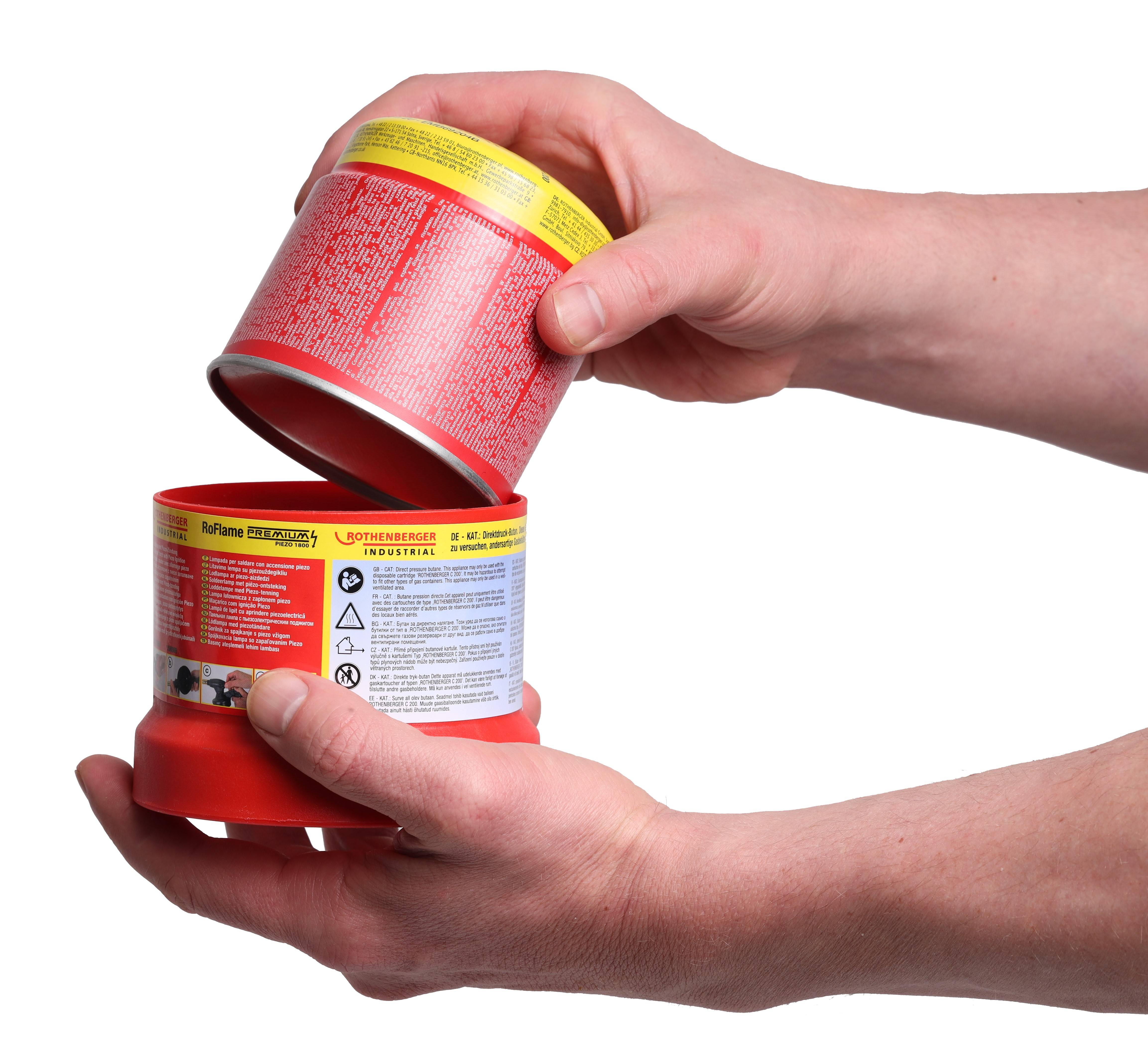 Eine Person hält eine geöffnete rote und gelbe Dose, die detaillierte Anweisungen sowohl auf dem Deckel als auch auf dem Behälter zeigt.