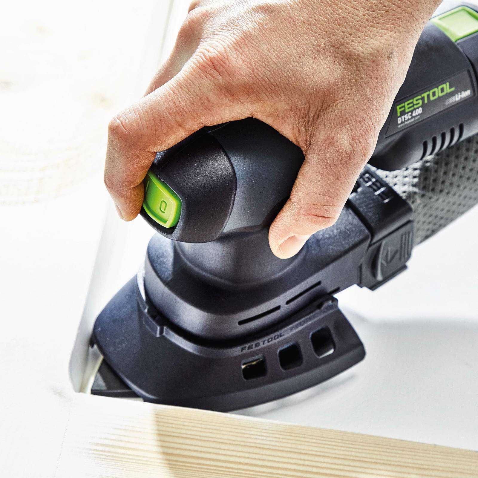 Eine Person verwendet einen tragbaren Festool DTS 400 Schleifer an einer Holzkante und demonstriert dabei das ergonomische Design und die Staubabsaugfähigkeit des Werkzeugs.