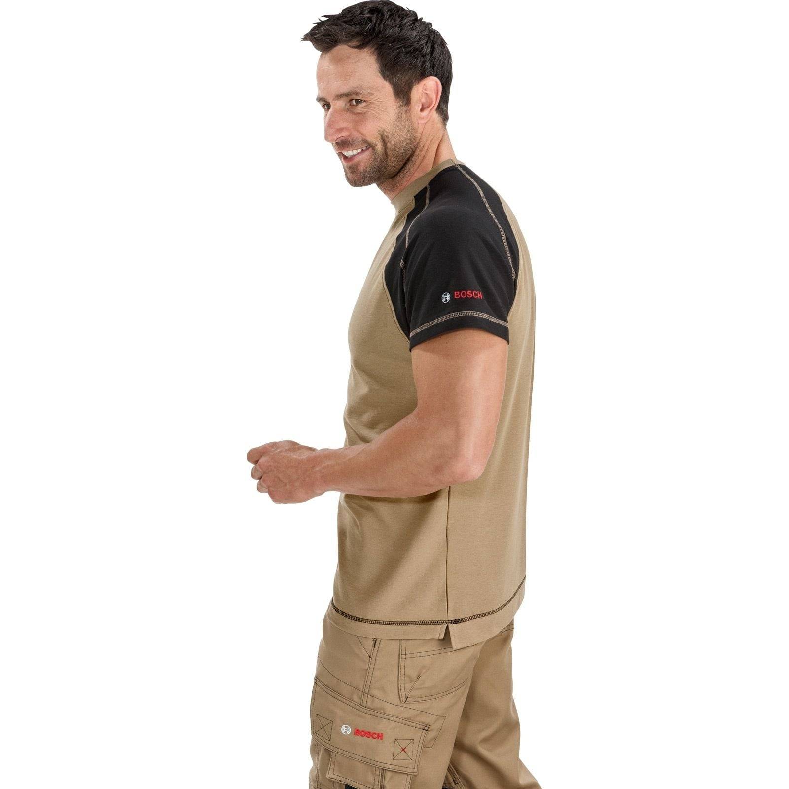 Ein Mann, der ein beige-schwarzes Arbeitshemd mit Bosch-Logos auf dem Ärmel und der Brust trägt, der seitlich blickt, vor einem weißen Hintergrund.