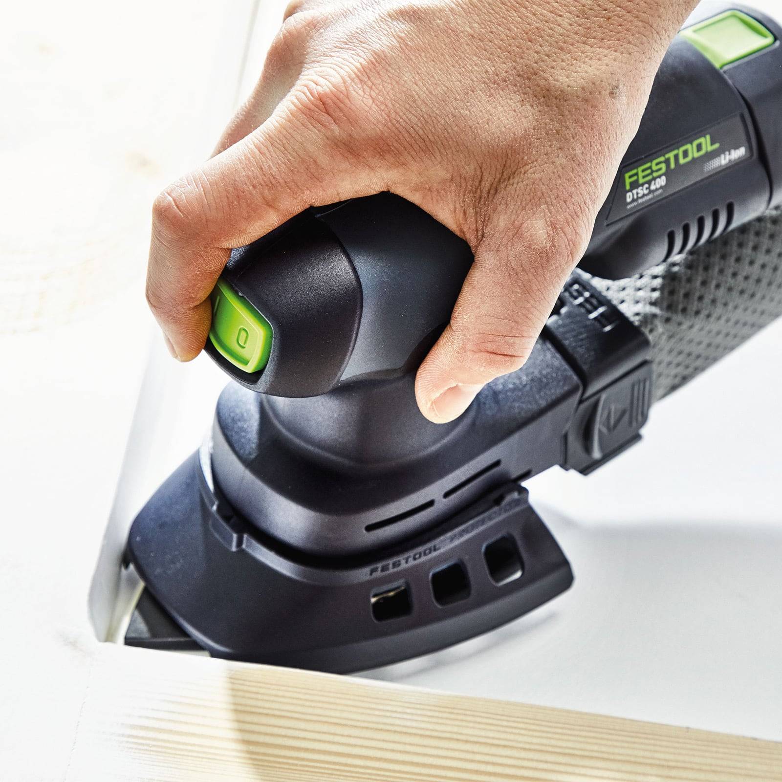 Eine Hand bedient eine Festool Akku-Schleifmaschine an einer weißen Holzkante und konzentriert sich dabei auf präzises Schleifen mit einem kleinen, kompakten Werkzeug.