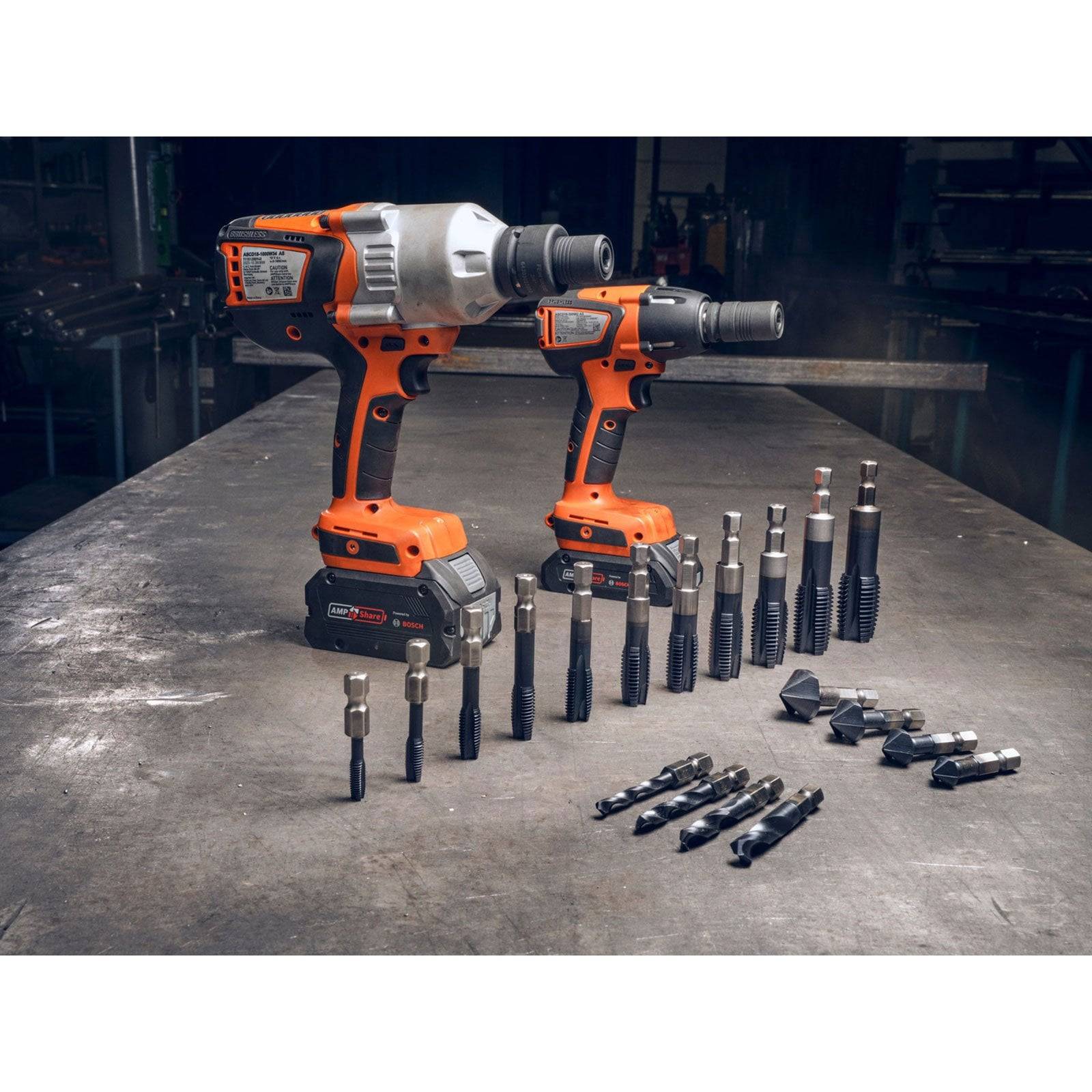 Zwei orange und schwarze Bohrmaschinen auf einem Metalltisch, umgeben von verschiedenen Bohrern und Zubehör in einer Werkstattumgebung.