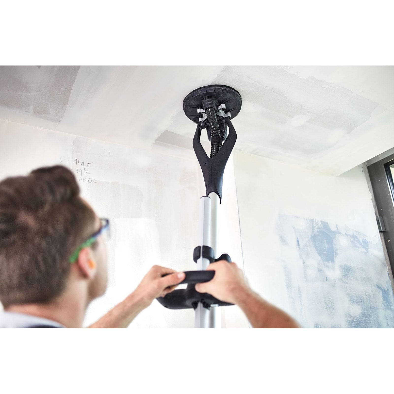 Eine Person verwendet ein Trockenbau-Schleifwerkzeug an einer Decke. Der Fokus liegt auf dem kreisförmigen Kopf des Werkzeugs, der die Deckenoberfläche berührt.