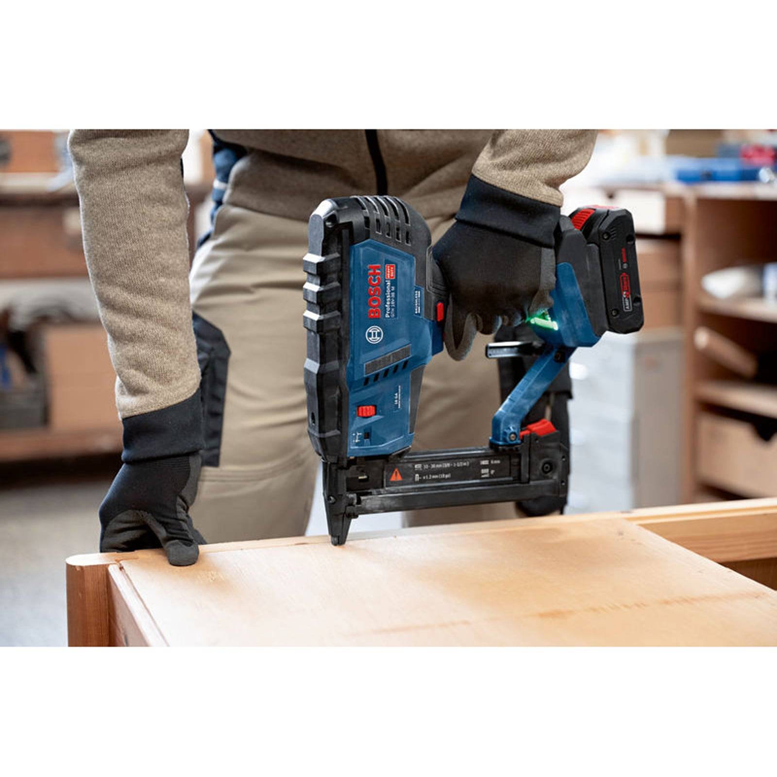 Person, der eine blaue kabellose Nagelschussmaschine auf einer Holzoberfläche in einer Werkstatt verwendet.