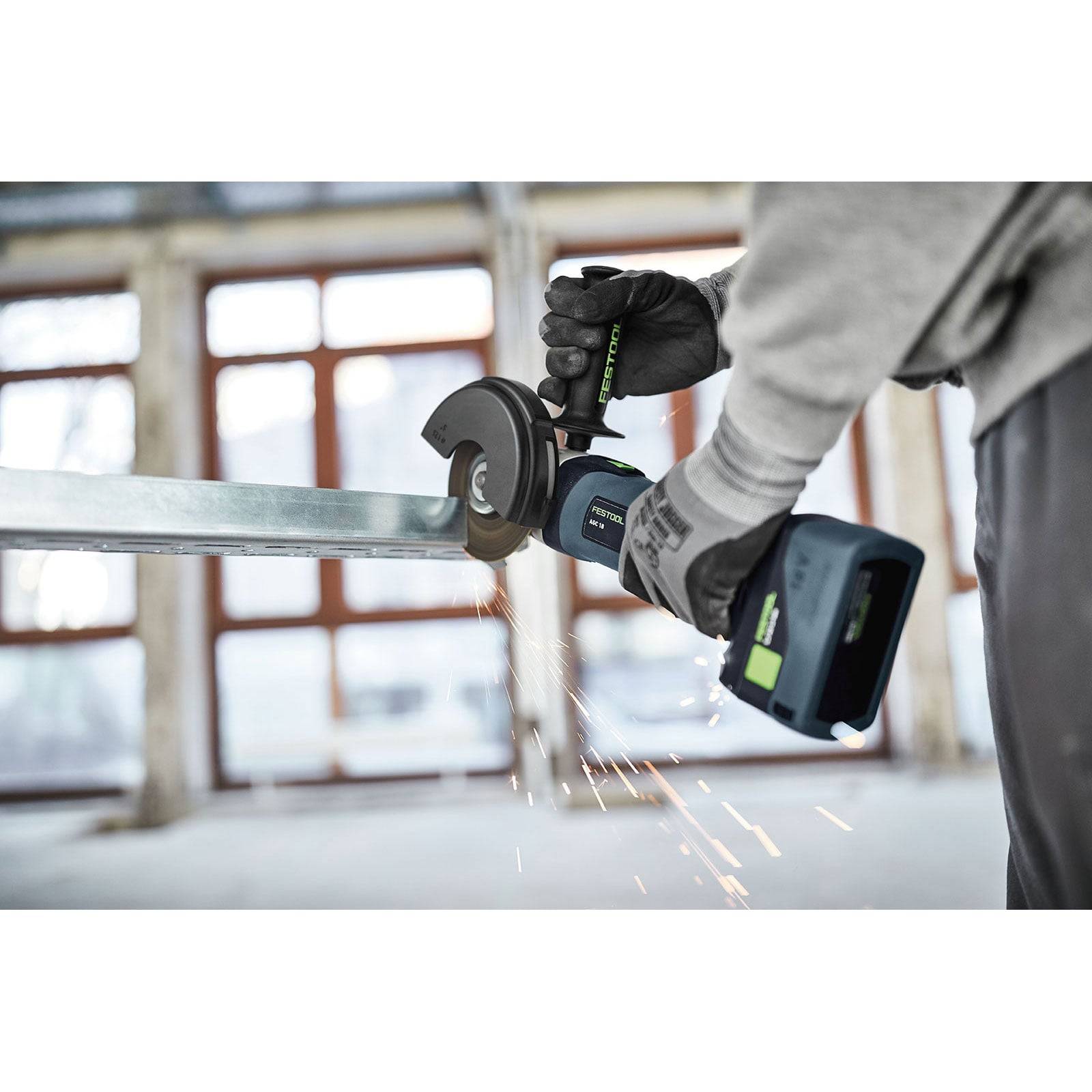 Eine Person verwendet eine Trennschleifmaschine, um einen Metallträger zu schneiden, wobei Funken sprühen, in einer Baustellenumgebung.