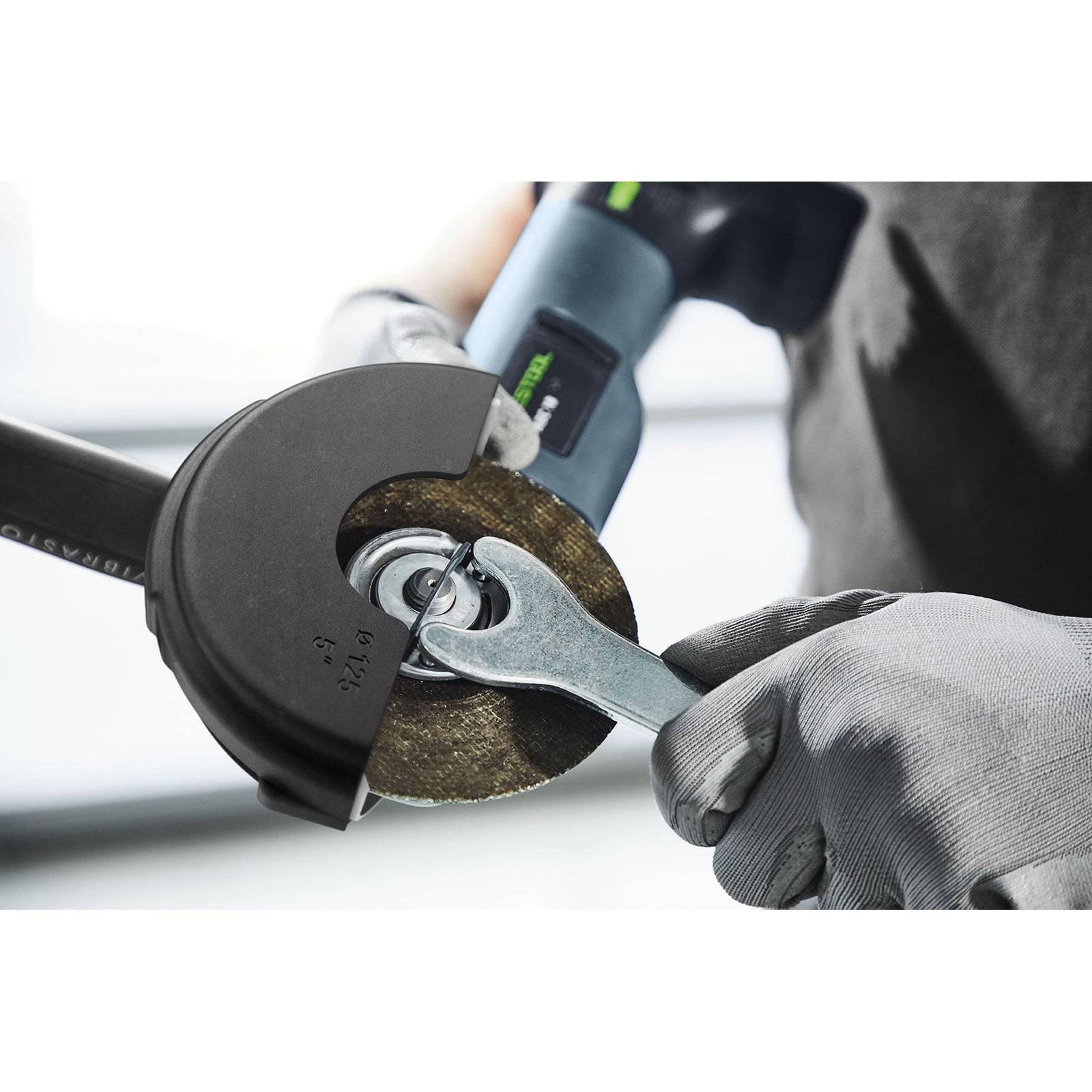 Eine Person mit Handschuhen bedient einen Schraubenschlüssel, um eine Scheibe an einer Winkelschleifer einzustellen.
