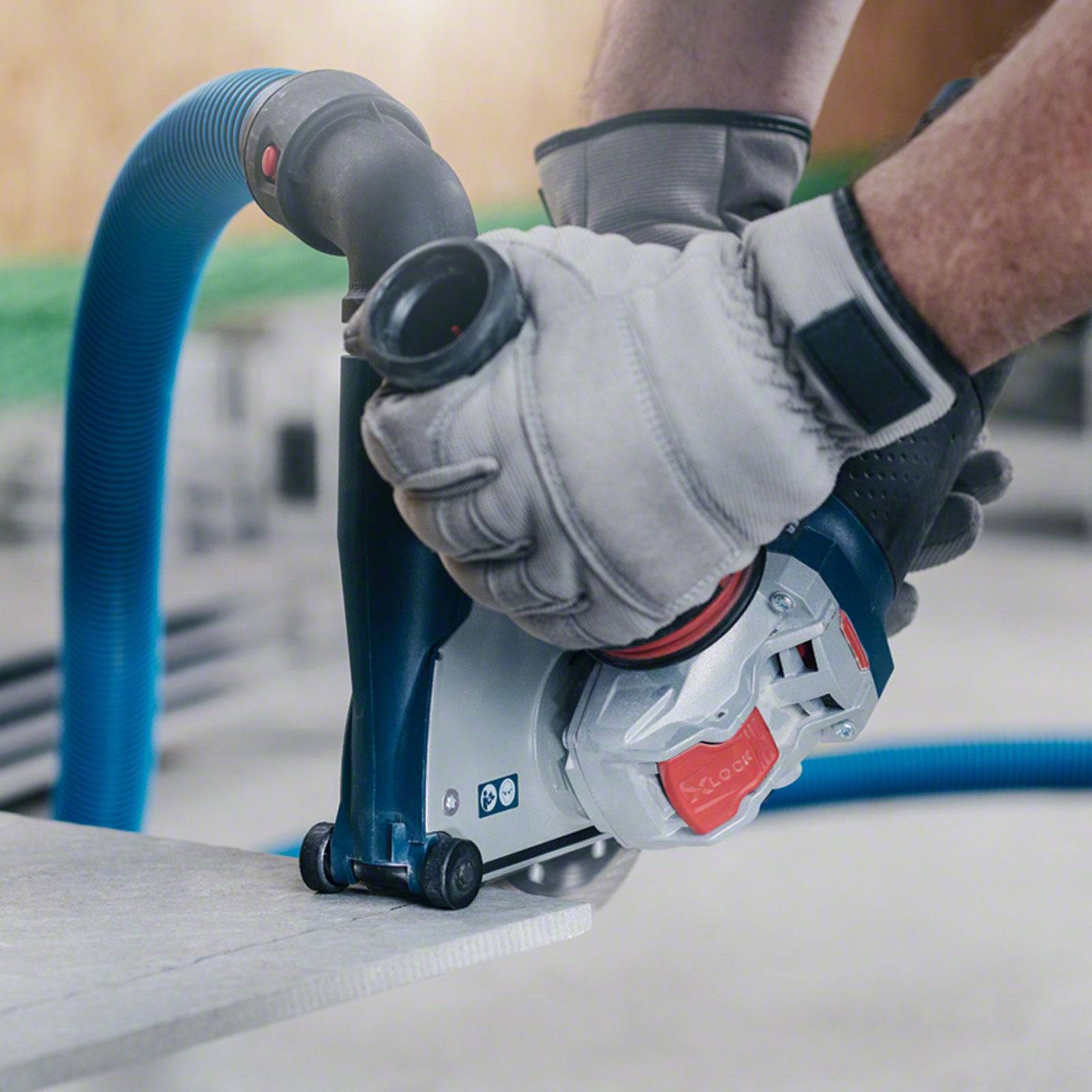 Eine Person mit Handschuhen verwendet ein Elektrowerkzeug mit angeschlossenem Absaughose, um eine Holzoberfläche im Innenbereich zu schleifen.