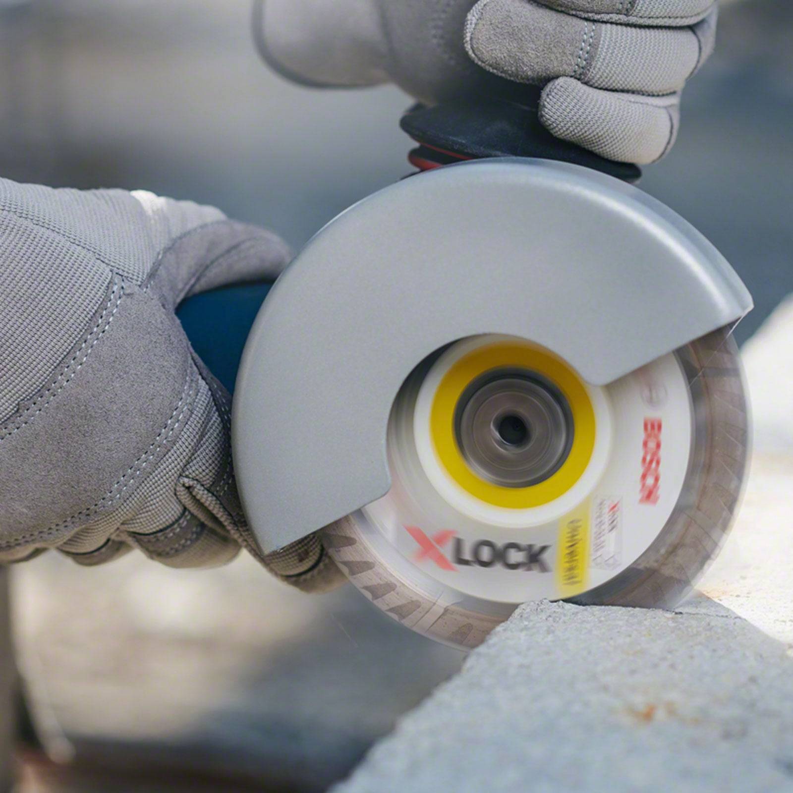 Eine Person mit Handschuhen benutzt einen Winkelschleiffer mit einem 'Bosch X-Lock'-Schleifblatt, um einen Betonblock zu schneiden.