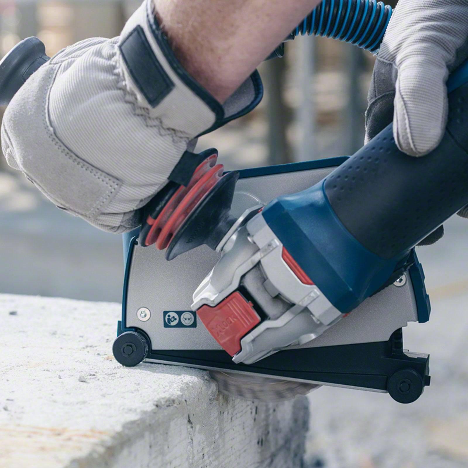 Eine Person verwendet eine elektrische Schleifmaschine auf einer Betonoberfläche und glättet die Kante. Das Werkzeug ist grau und blau mit einem roten Sicherheitsknopf.