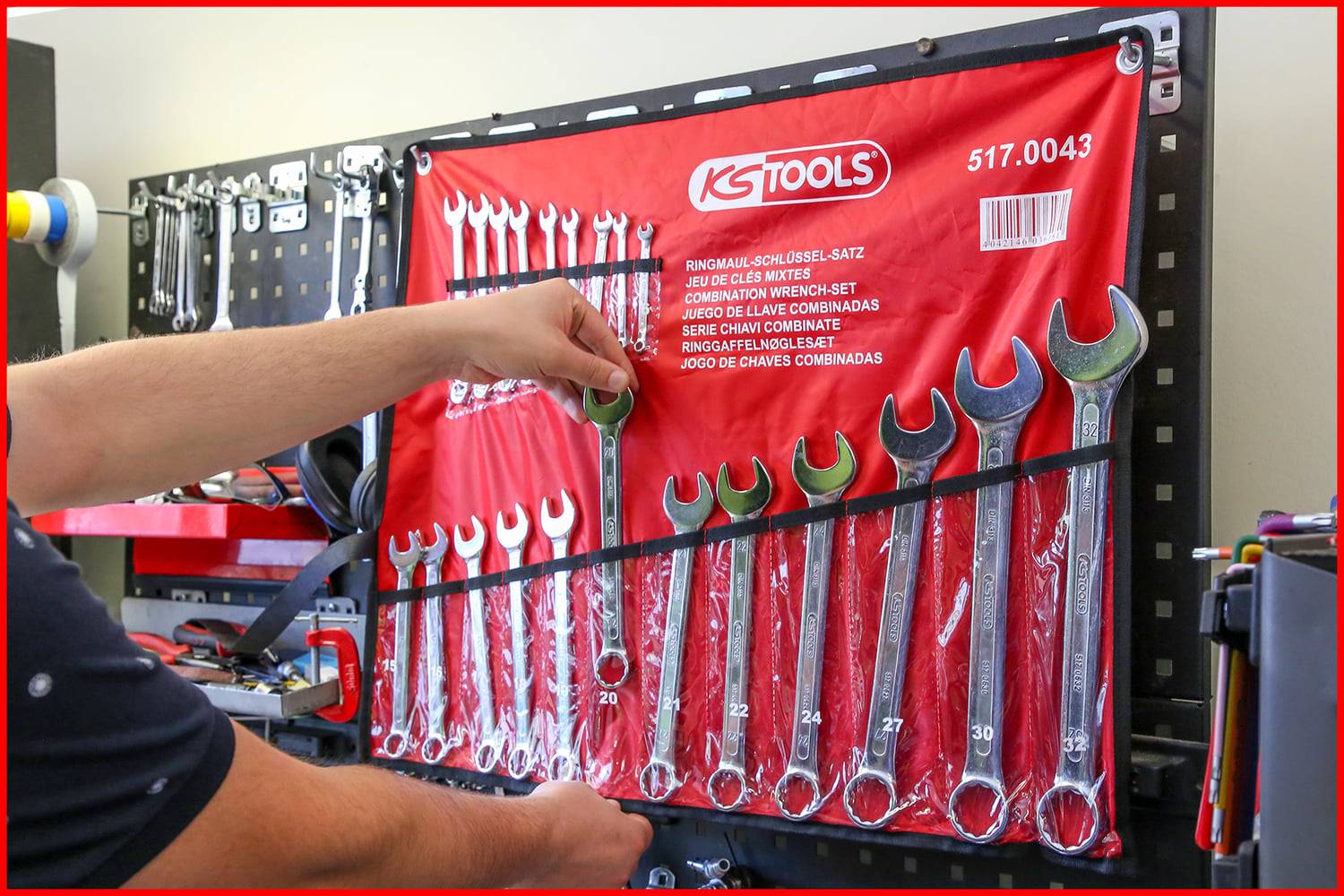 Eine Person wählt einen Schraubenschlüssel aus einem wandmontiertem KS Tools Schraubenschlüsselsatz aus, der nach Größe nummeriert ist und von 6 bis 36 reicht, an einem roten Werkzeughalter.